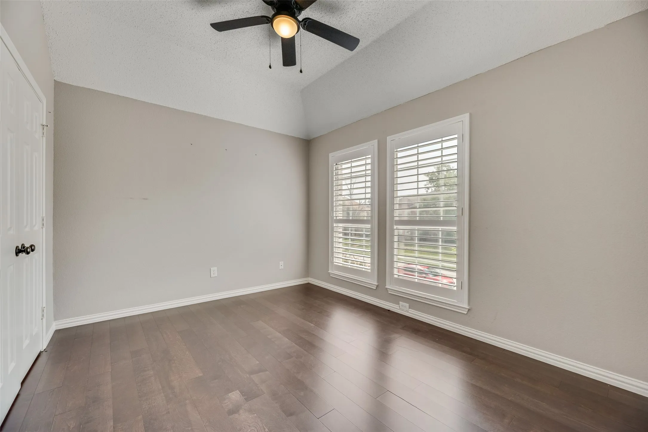Vaulted ceiling with a ceiling fan, wood-finish flooring, and dual windows with plantation shutters