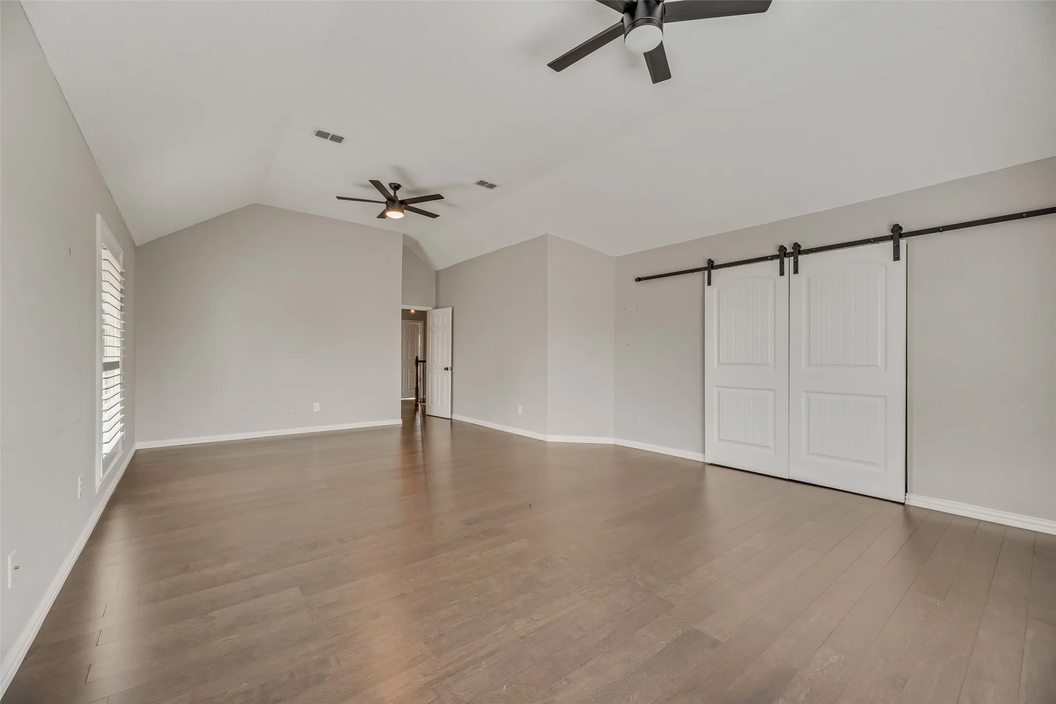 Vaulted ceiling with dual ceiling fans, wood-finish flooring, plantation shutters, and sliding barn​​‌​​​​‌​​‌‌​‌‌​​​‌‌​‌​‌​‌​​​‌​​ doors