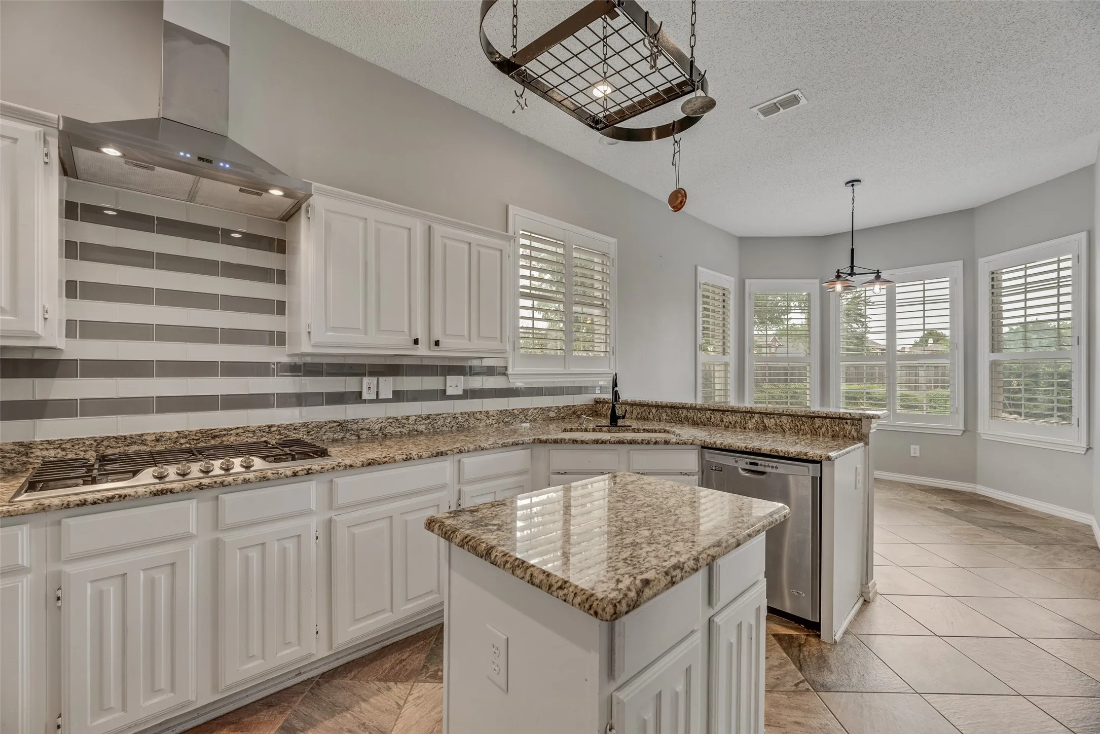 Kitchen featuring white cabinetry, granite countertops, stainless steel appliances, a tile backsplash, and a bay window with plantation shutters