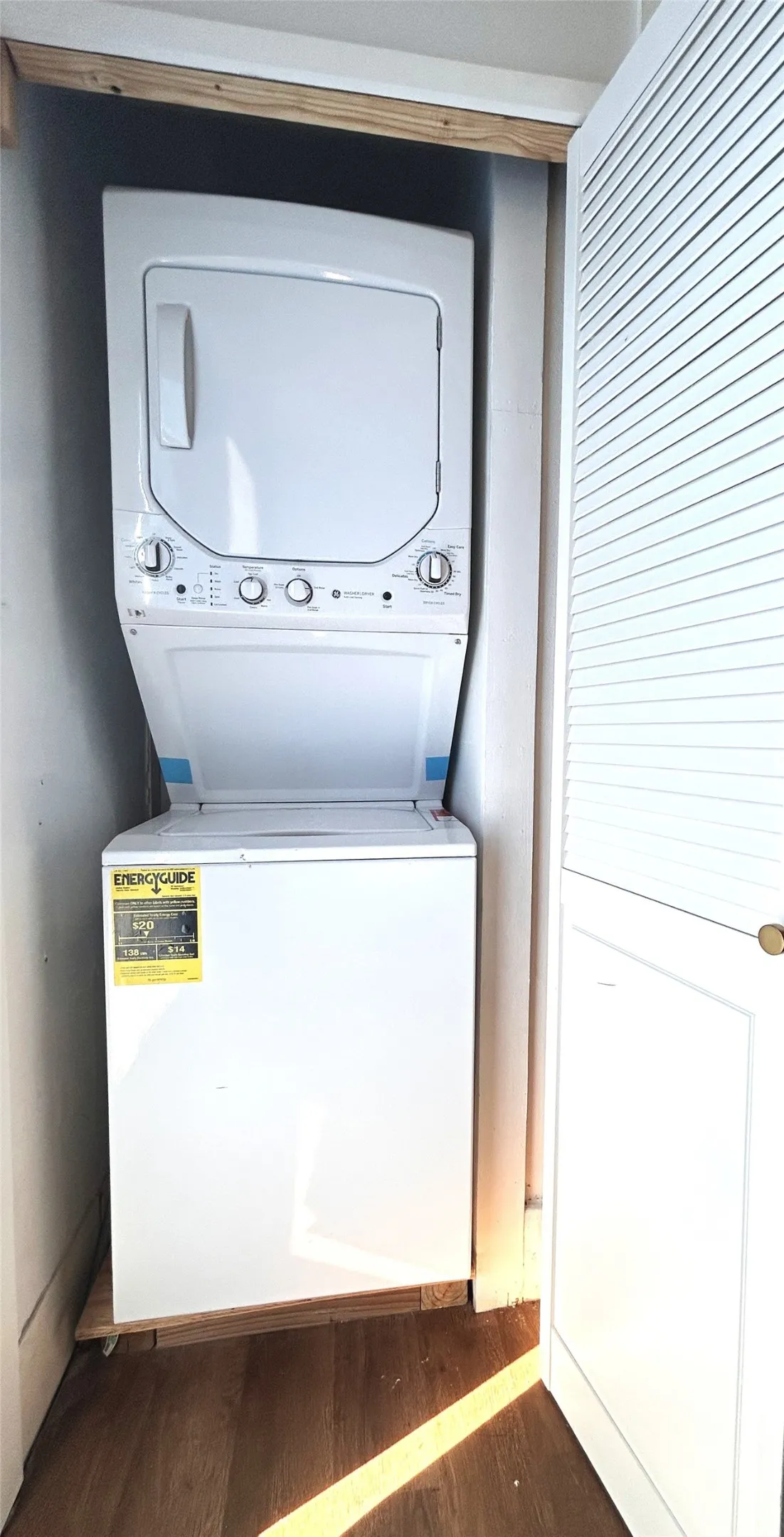 Built-in stackable washer and dryer unit within a closet, featuring louvered bi-fold doors and wood-finish flooring
