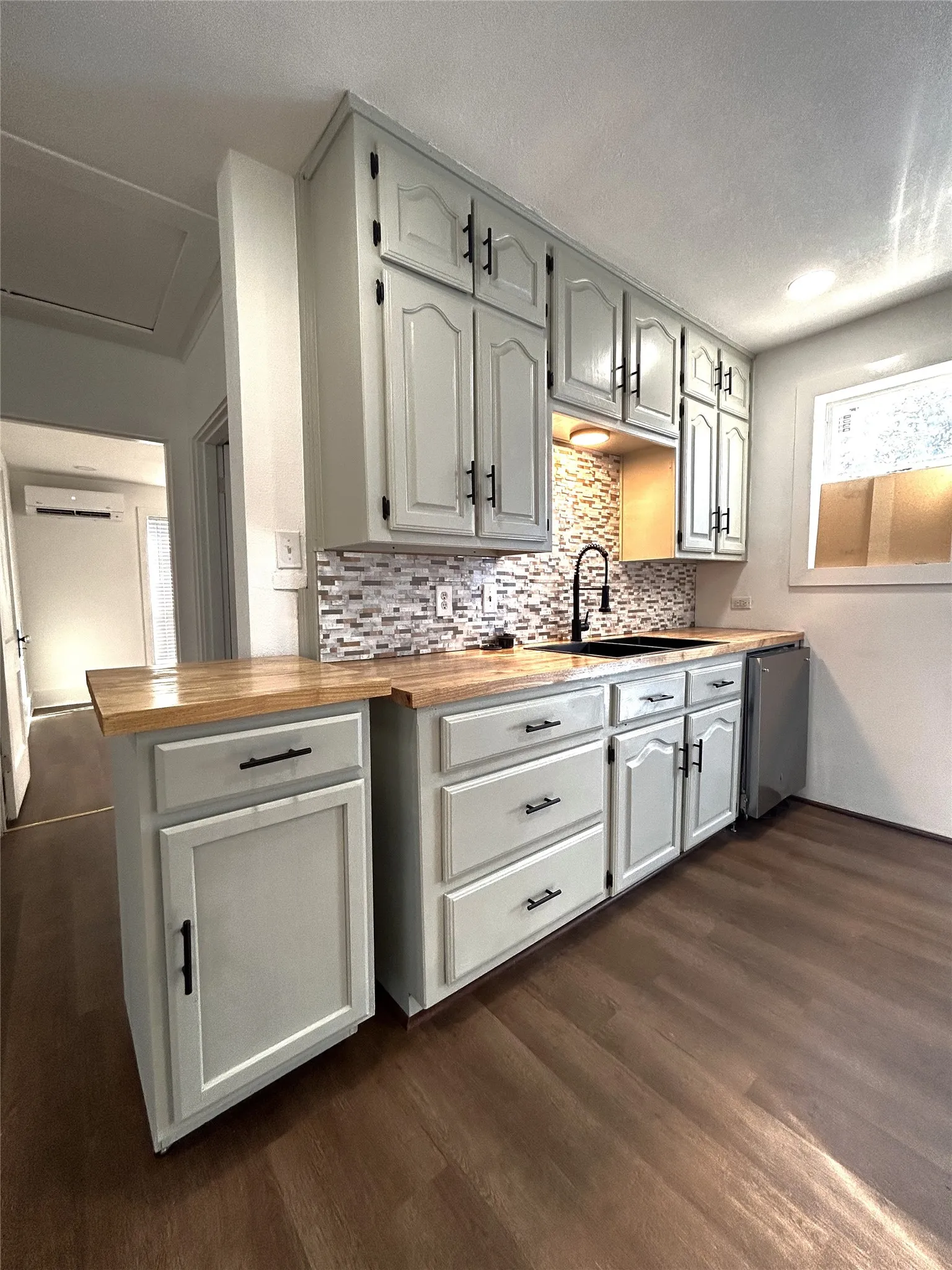Light-toned cabinetry with black hardware, wood-finish countertops, mosaic tile backsplash, matte black gooseneck faucet, and wood-finish flooring