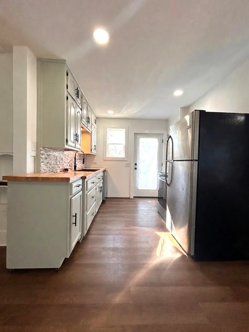 Galley kitchen with light-toned cabinetry, wood butcher block countertops, stainless steel appliances, and wood-finish flooring
