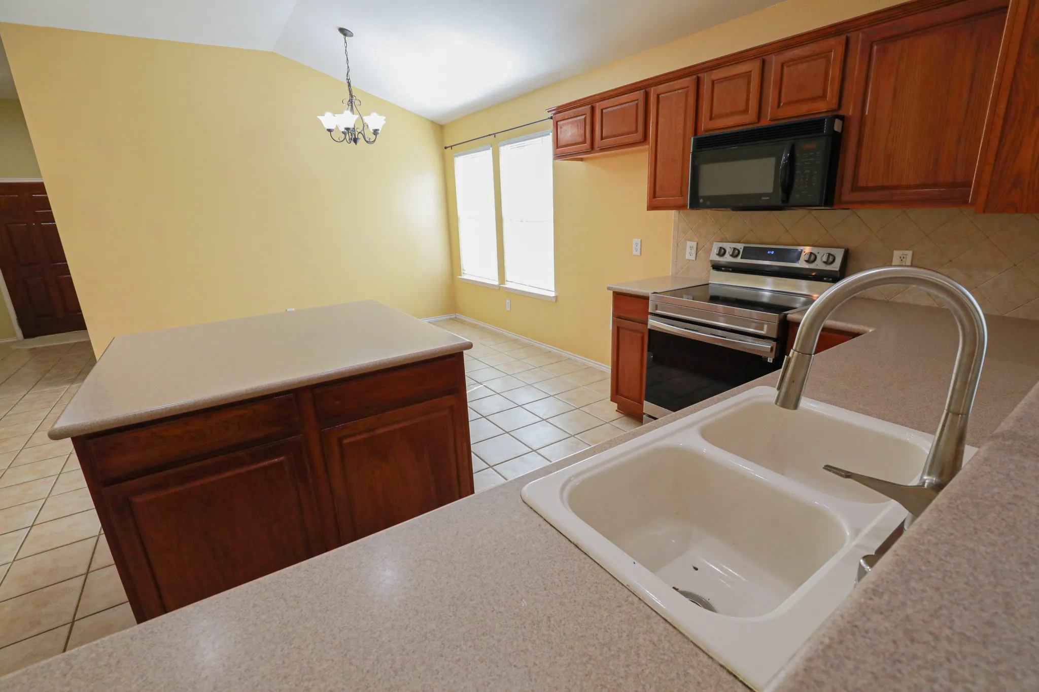 Kitchen with wood-finish cabinetry, solid surface countertops, a double basin sink, and tile flooring