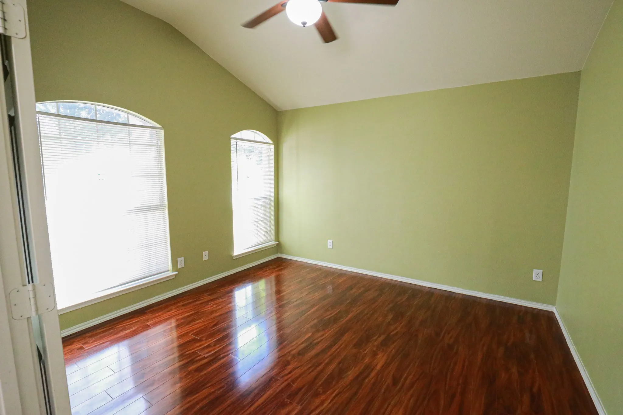 Vaulted ceiling with a ceiling fan, two arched windows, and wood-finish flooring