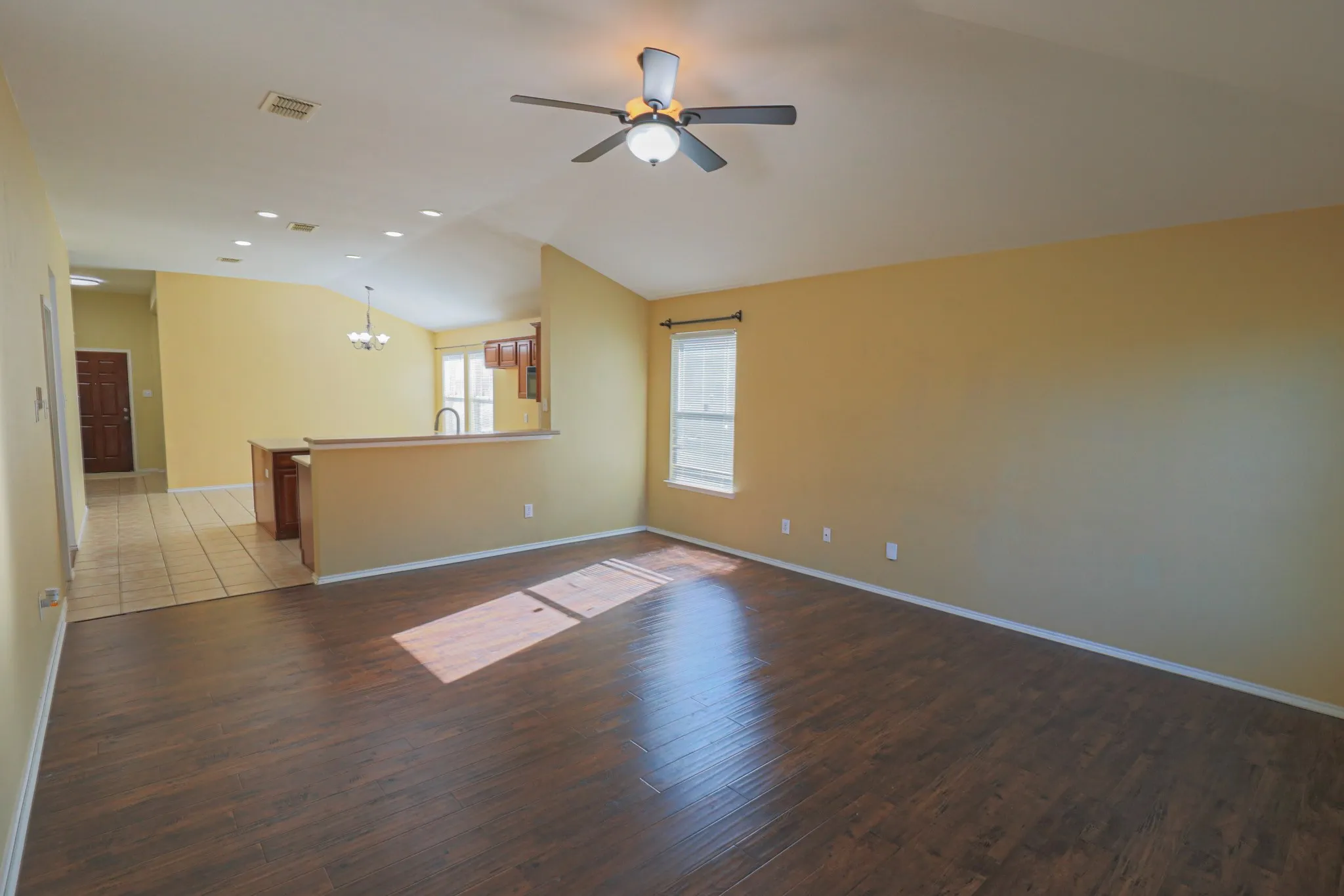Vaulted ceiling with a ceiling fan, wood-finish flooring, recessed lighting, and a kitchen pass-through with wood-finish cabinetry