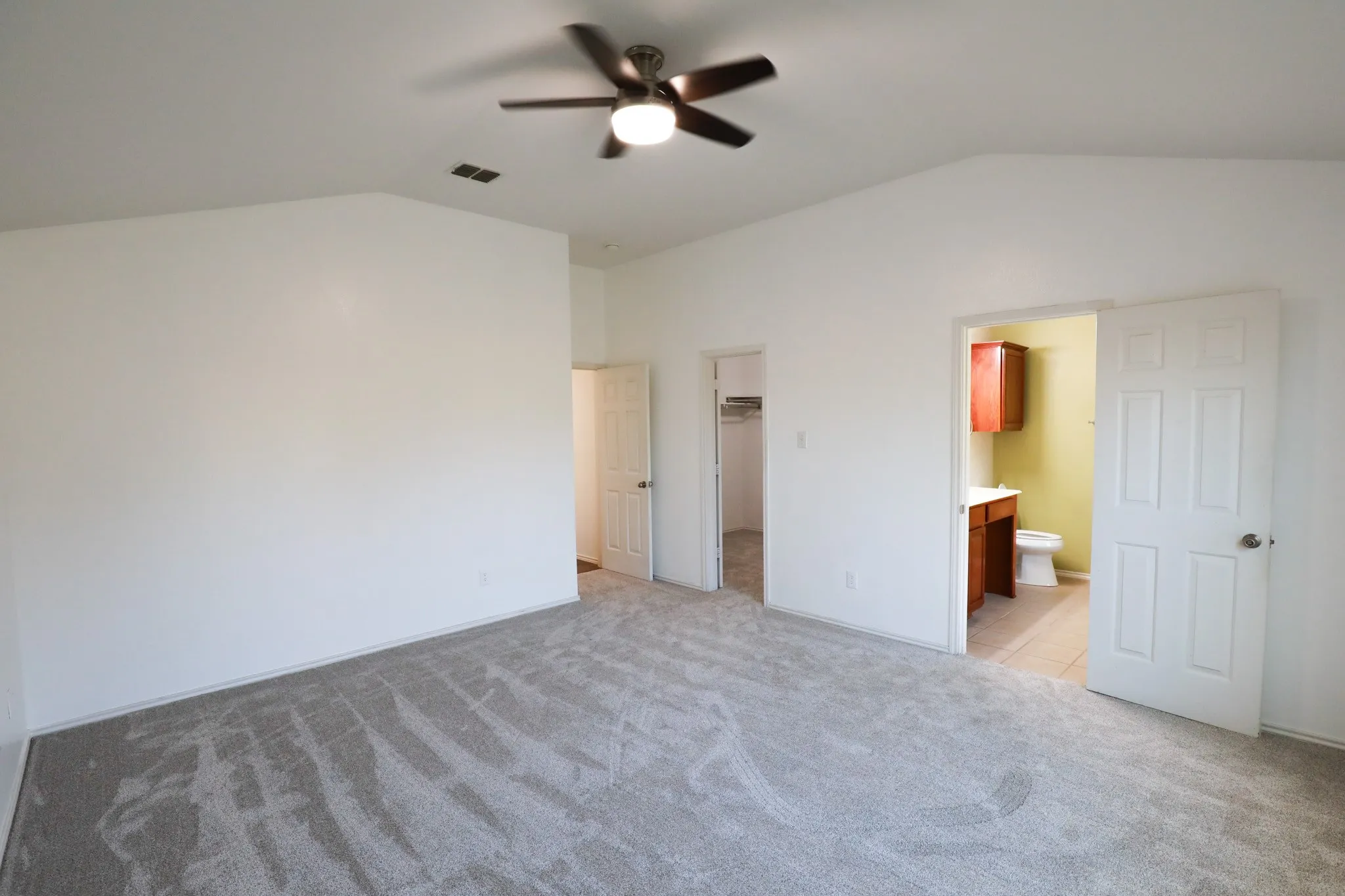Vaulted ceiling with a ceiling fan, carpeted flooring, and a built-in vanity in the adjacent room