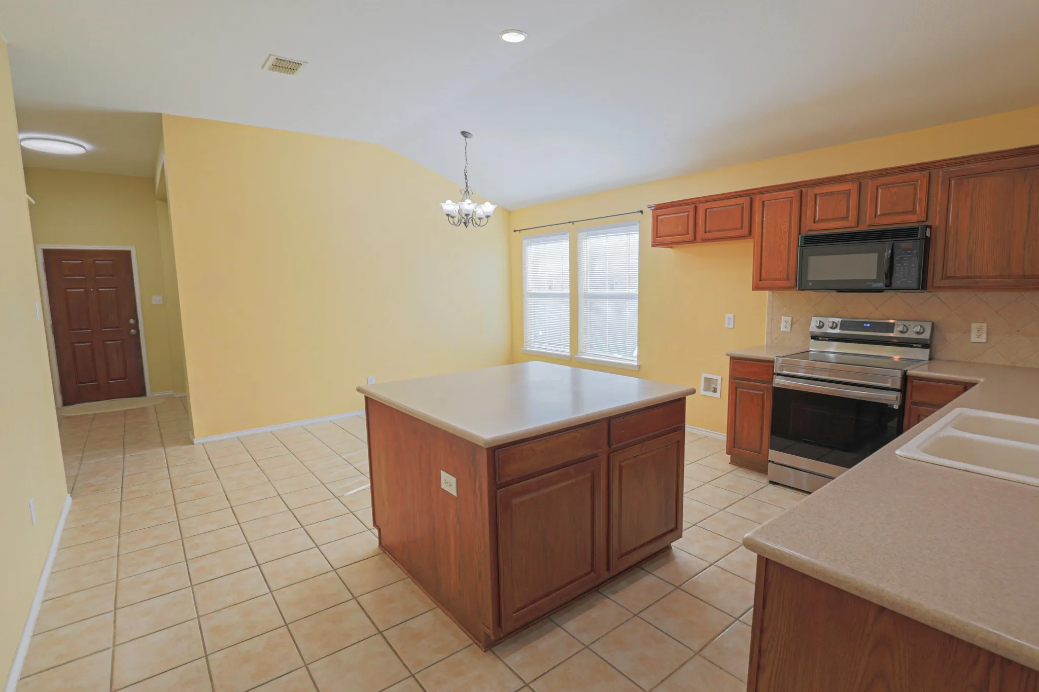 Kitchen featuring a central island, wood-finish cabinetry, stainless steel appliances, tile flooring, and a double basin sink