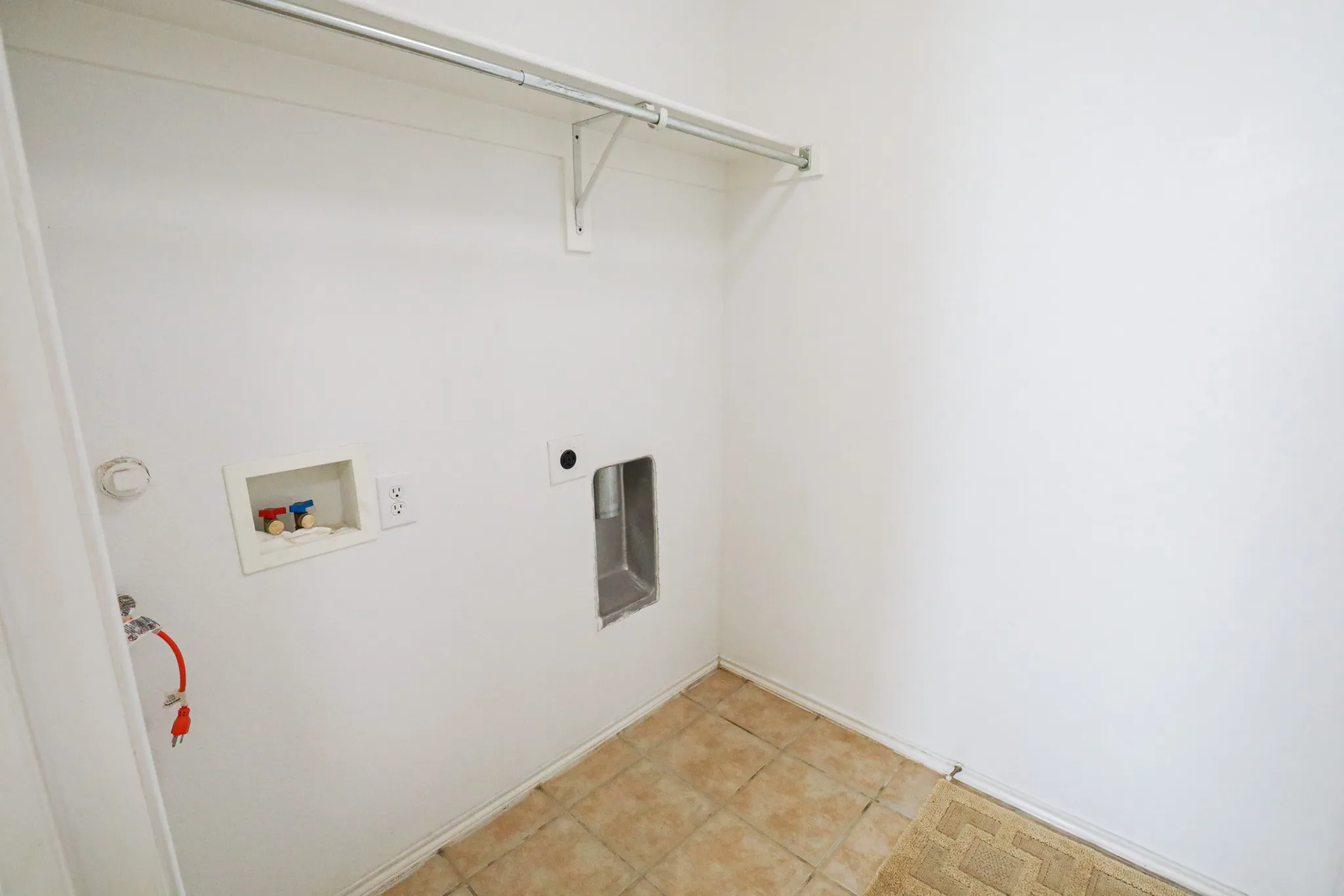 Utility space with tile flooring, wall-mounted water hookups, and a built-in hanging rod