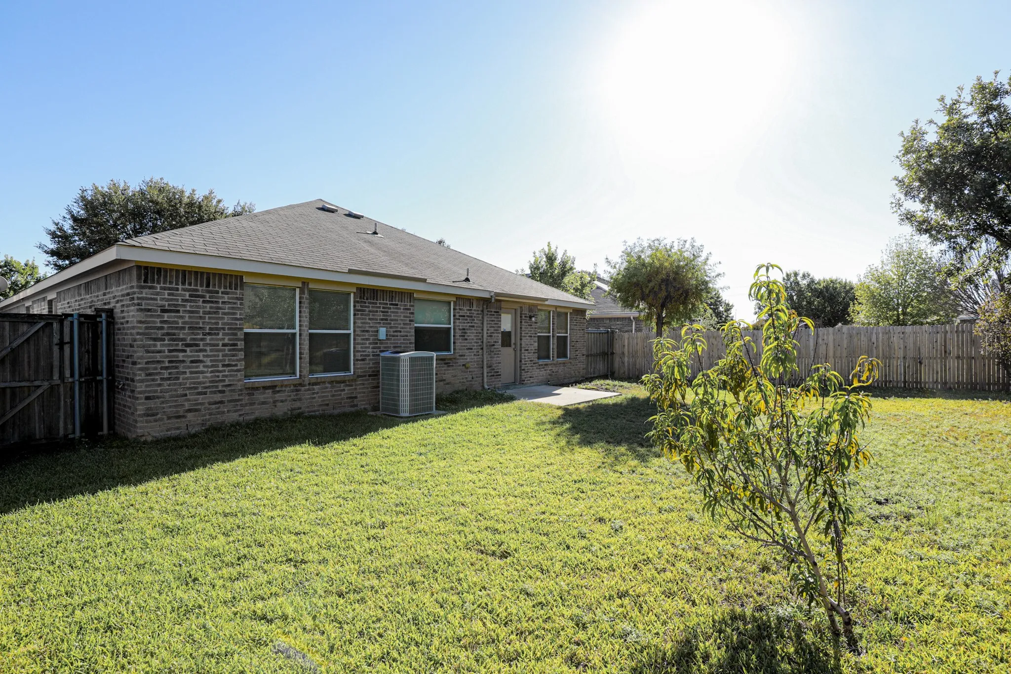 Expansive backyard featuring a manicured lawn, brick exterior, and a privacy fence