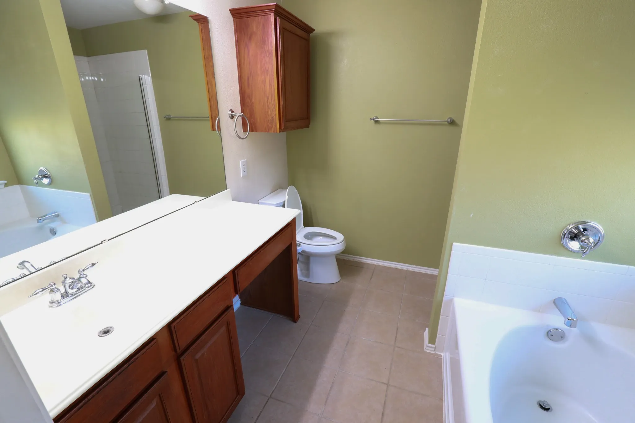 Dual-sink vanity with wood-finish cabinetry, a framed mirror, and tile flooring