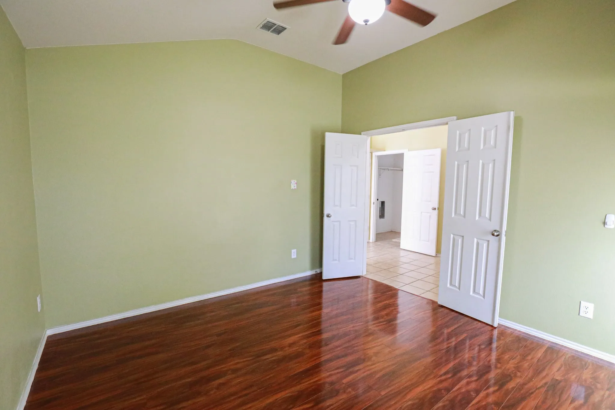 Varnished wood-finish flooring, vaulted ceiling, and ceiling fan with integrated lighting