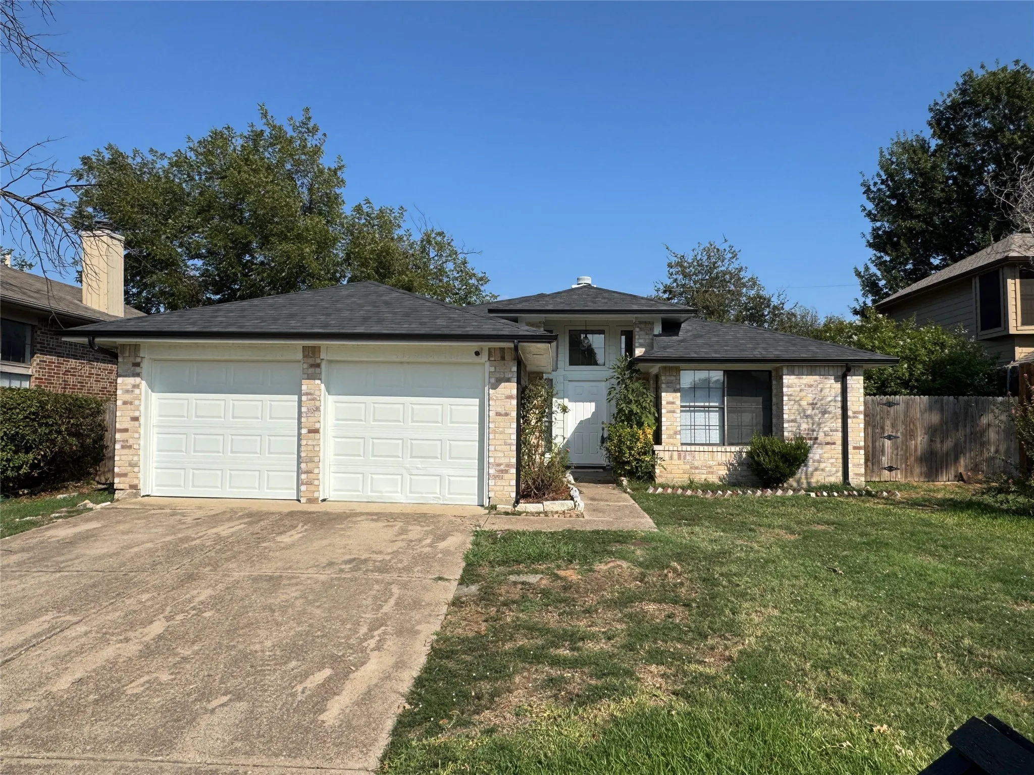 Brick veneer exterior with a two-car garage, mature landscaping, and a fenced yard