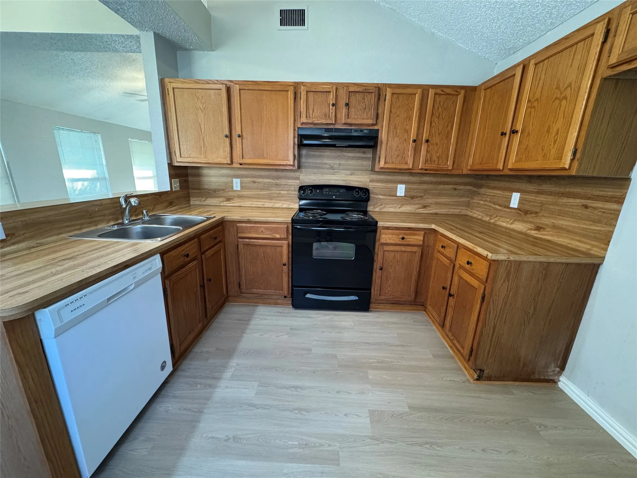 Kitchen featuring wood-finish cabinetry, wood-finish countertops, black range, white dishwasher, and light-toned flooring