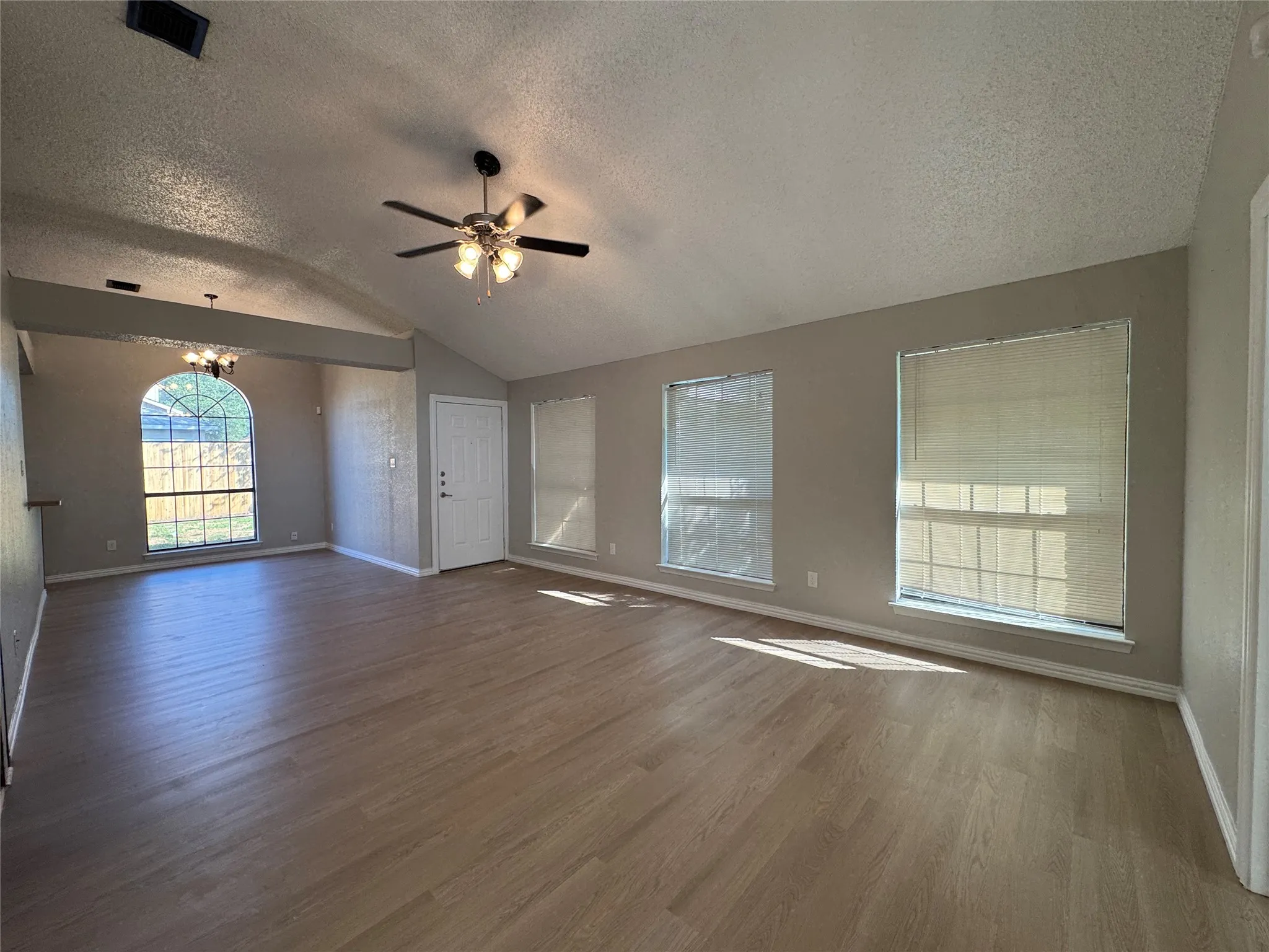 Vaulted ceiling, wood-finish flooring, ceiling fan, arched window, and multiple windows