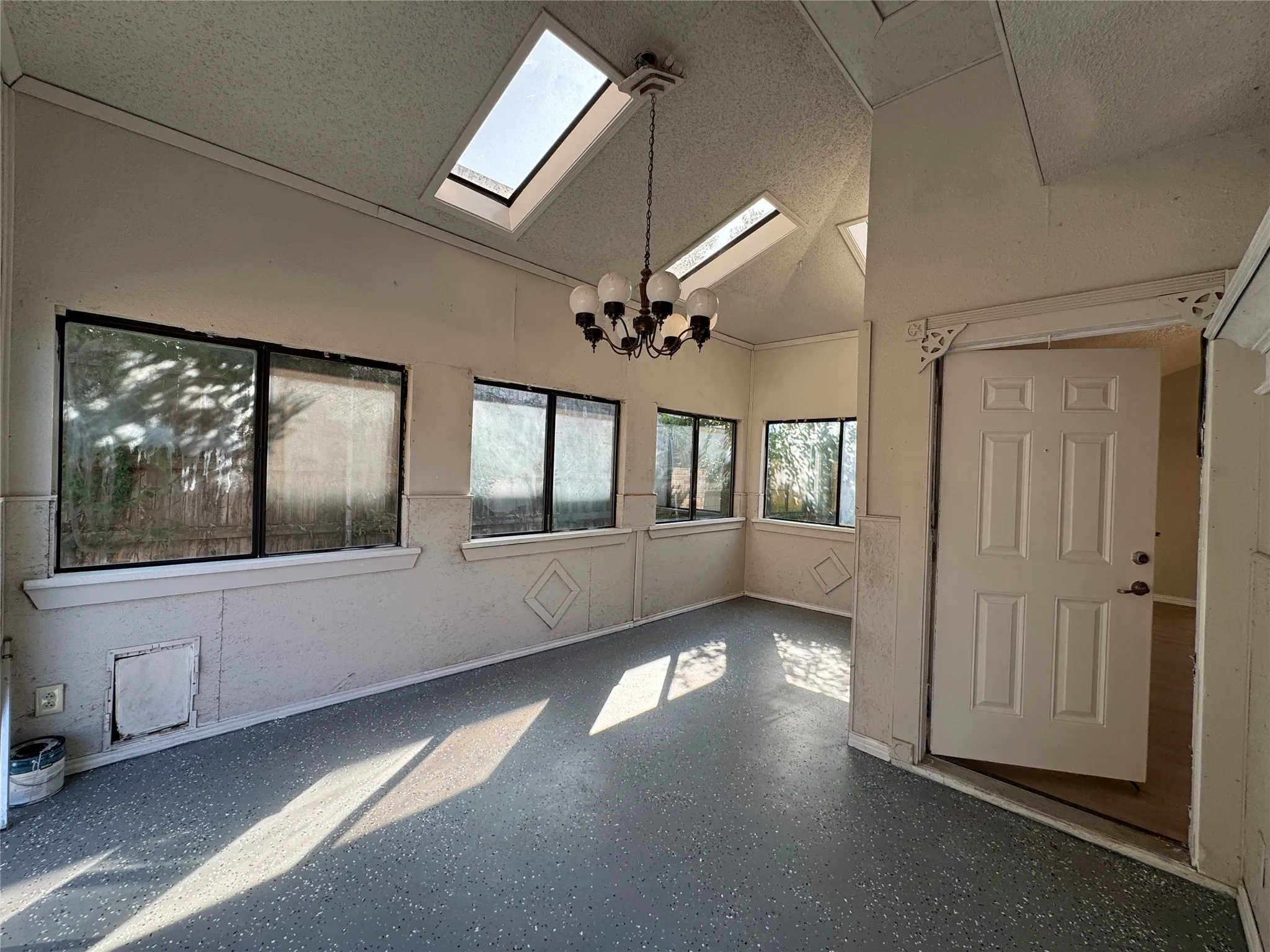 Vaulted ceiling with skylights, multiple windows, textured walls, and a multi-light chandelier