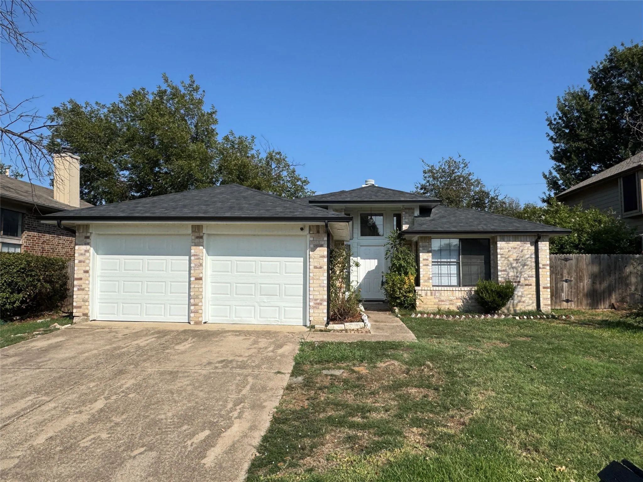 Brick exterior with a dark-shingle roof, featuring a two-car garage, established landscaping, and a concrete driveway