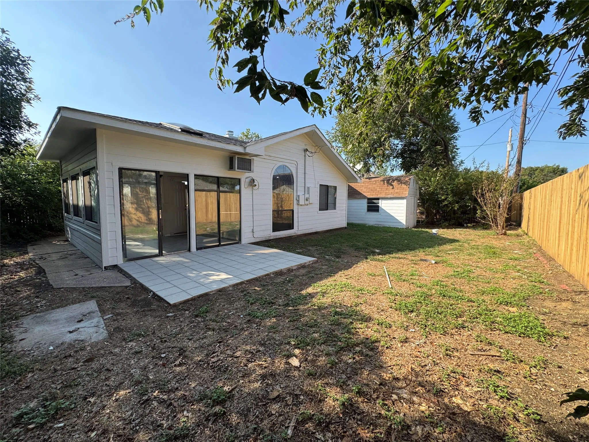 Expansive backyard featuring a wood fence, detached storage shed, and a tiled patio with sliding glass doors
