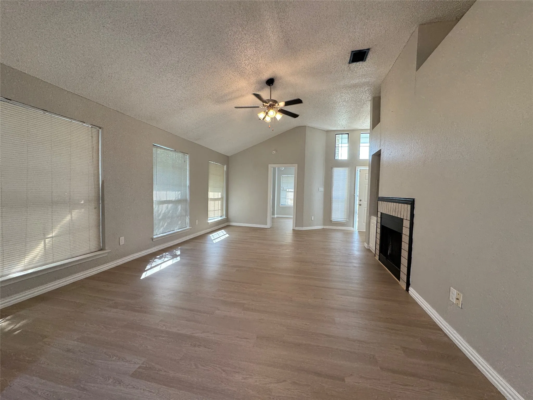 Vaulted ceiling with an attached ceiling fan, wood-finish flooring, and a fireplace with a tiled surround