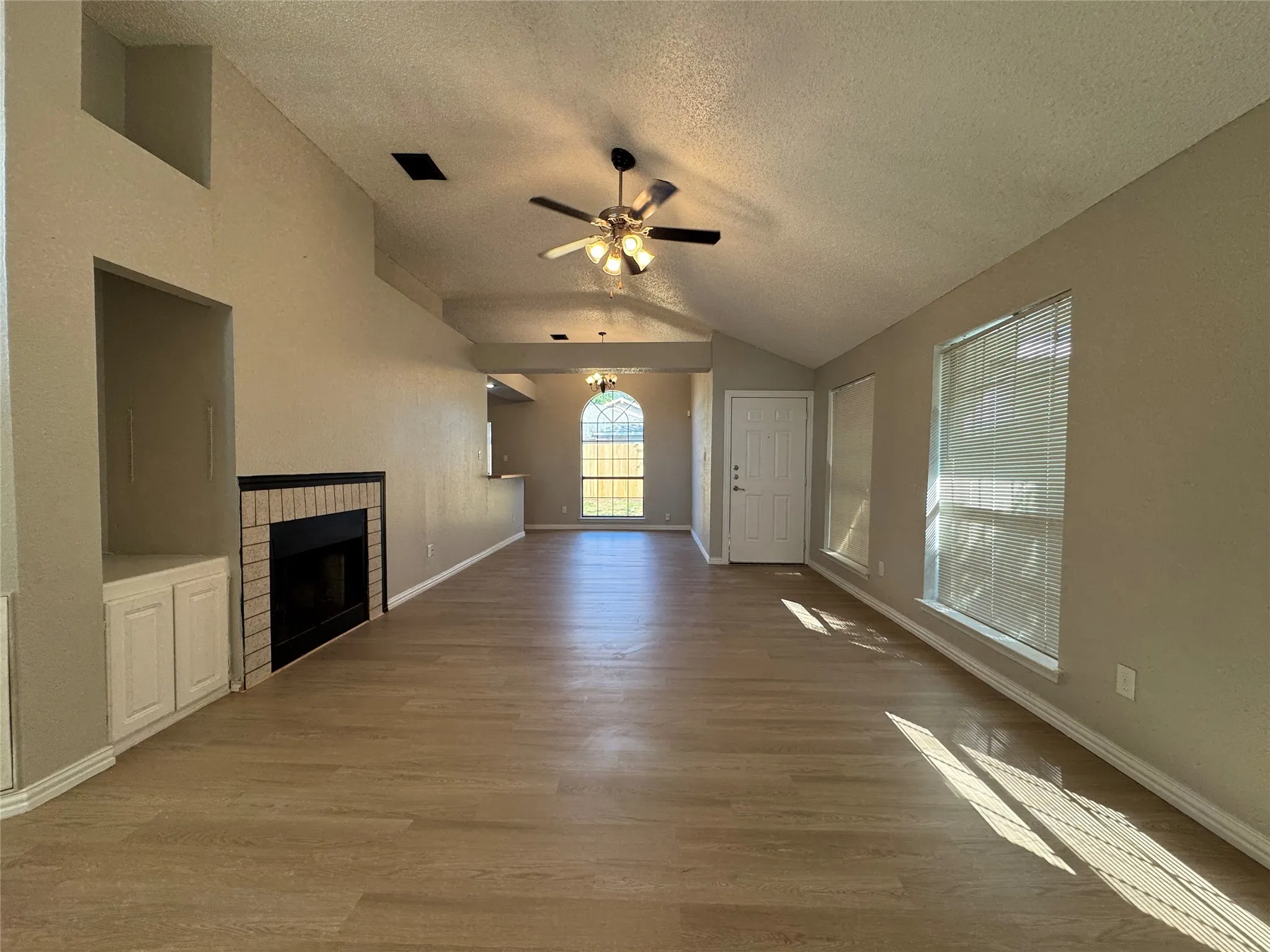 Vaulted ceilings, wood-finish flooring, brick fireplace surround, built-in cabinetry, and multiple windows