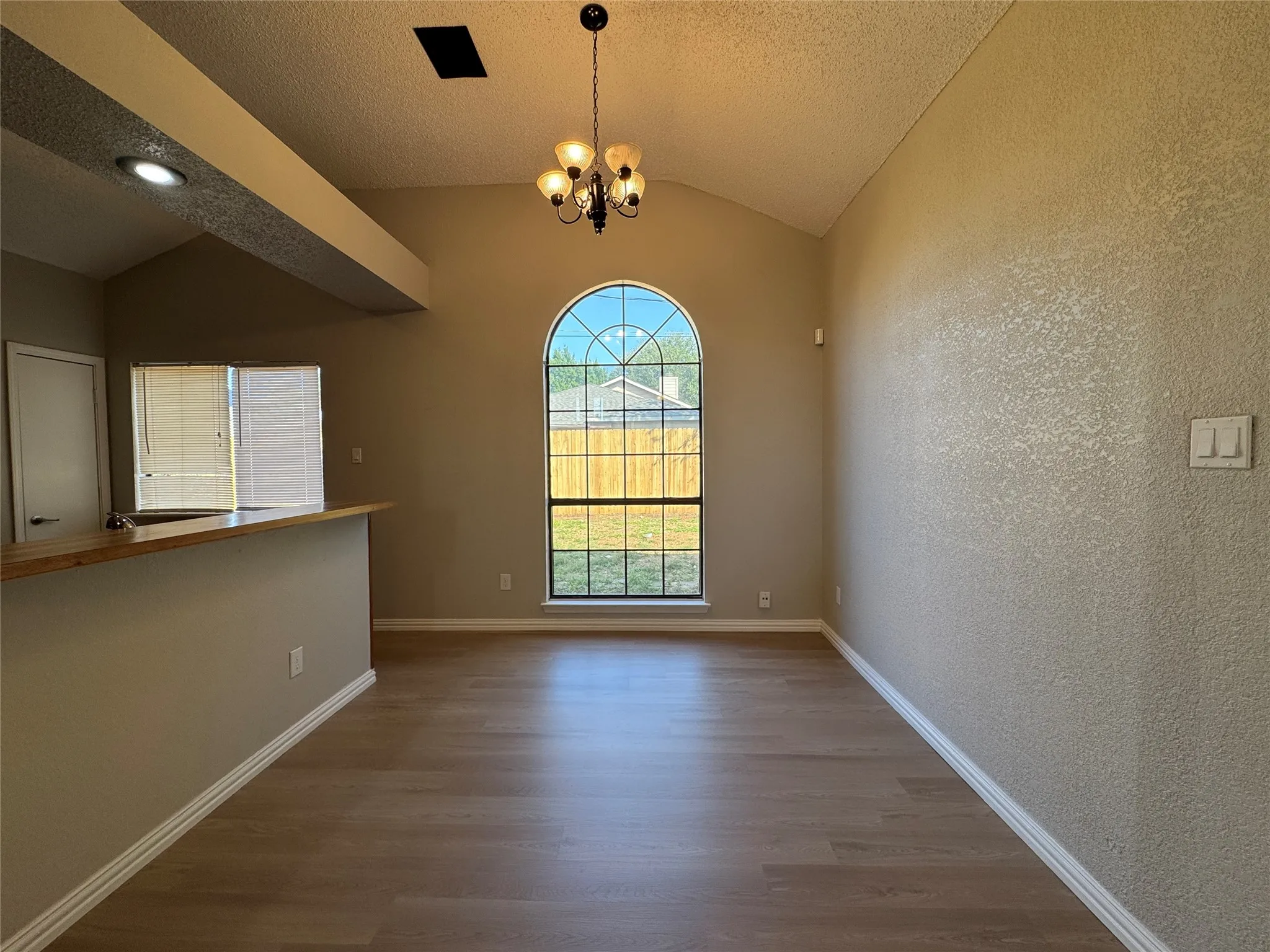 Vaulted ceiling with an arched window, wood-finish flooring, and a breakfast bar with wood-finish countertop