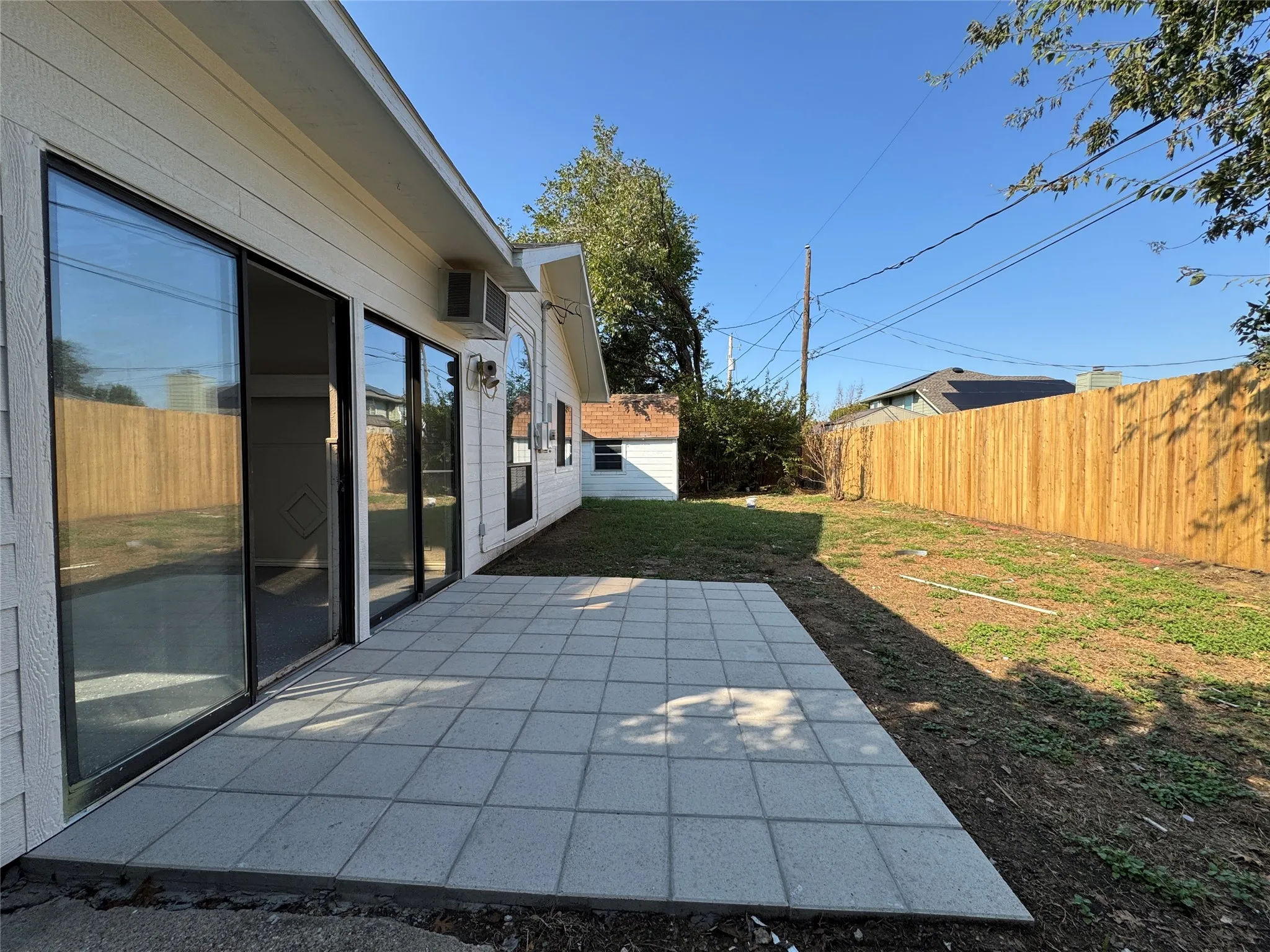 Rear exterior featuring a concrete paver patio, sliding glass doors, and a wood privacy fence
