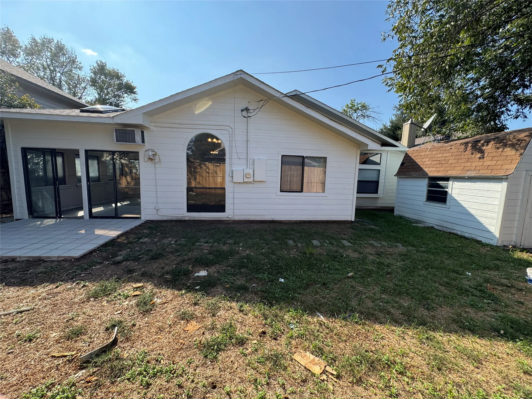 White siding exterior with a pitched roof, arched window, and glass panel doors