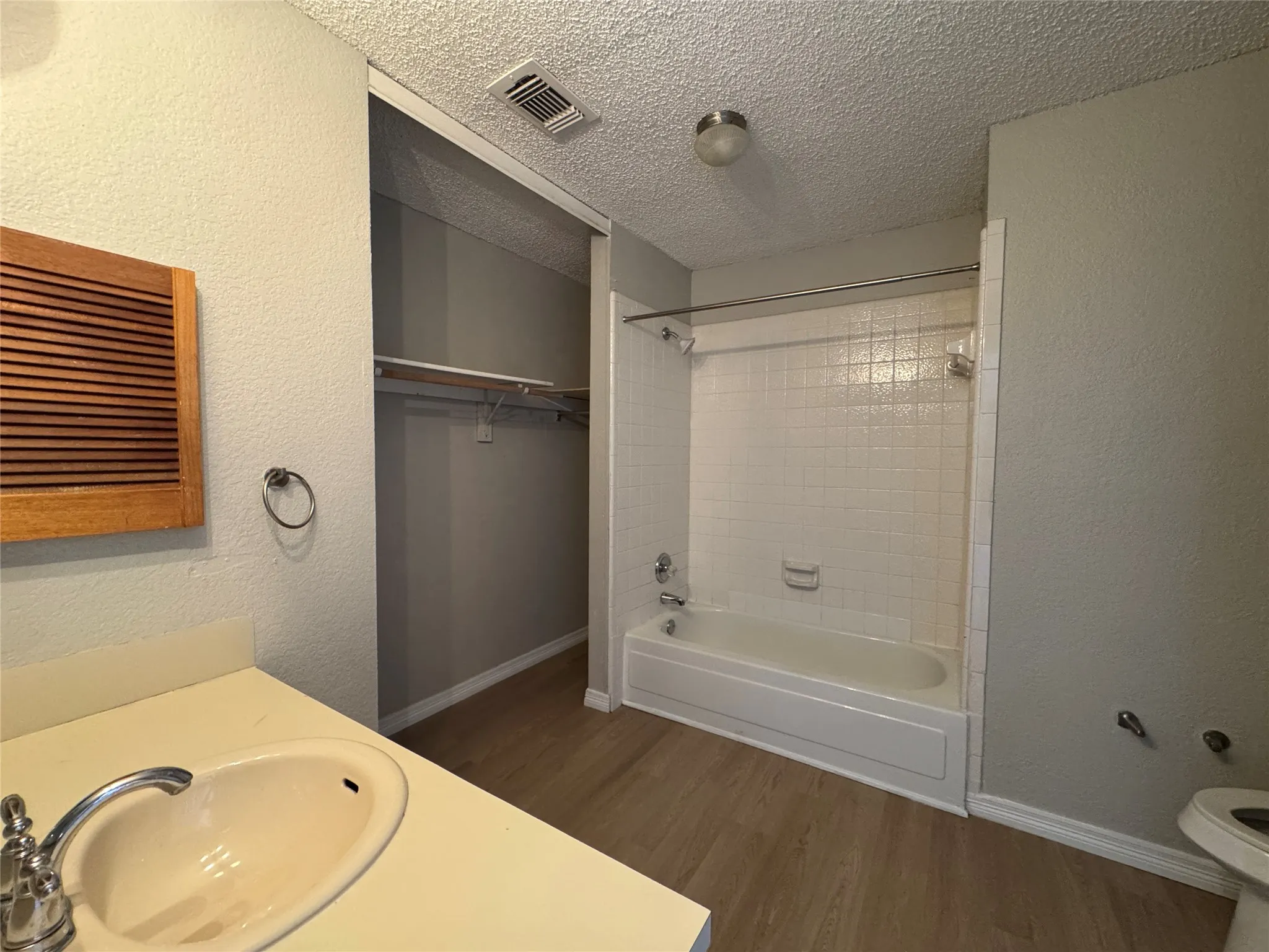 Vanity with an integrated sink and chrome faucet, wood-finish flooring, white tiled shower and tub combination, and an open closet