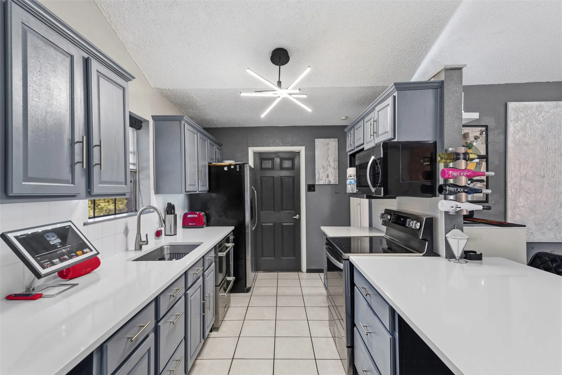 Galley kitchen with white tile flooring, gray cabinetry, white countertops, built-in stainless steel appliances, and a modern ceiling light fixture