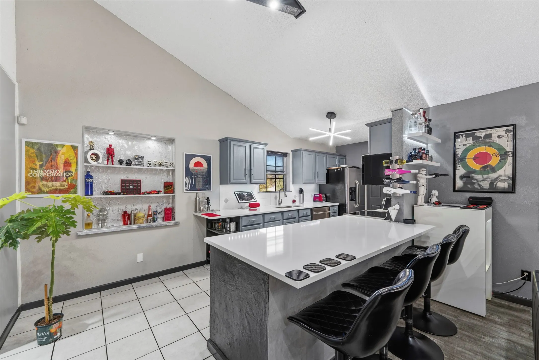 Kitchen featuring a vaulted ceiling, recessed shelving with integrated lighting, a central island with countertop seating, gray cabinetry, and tiled flooring