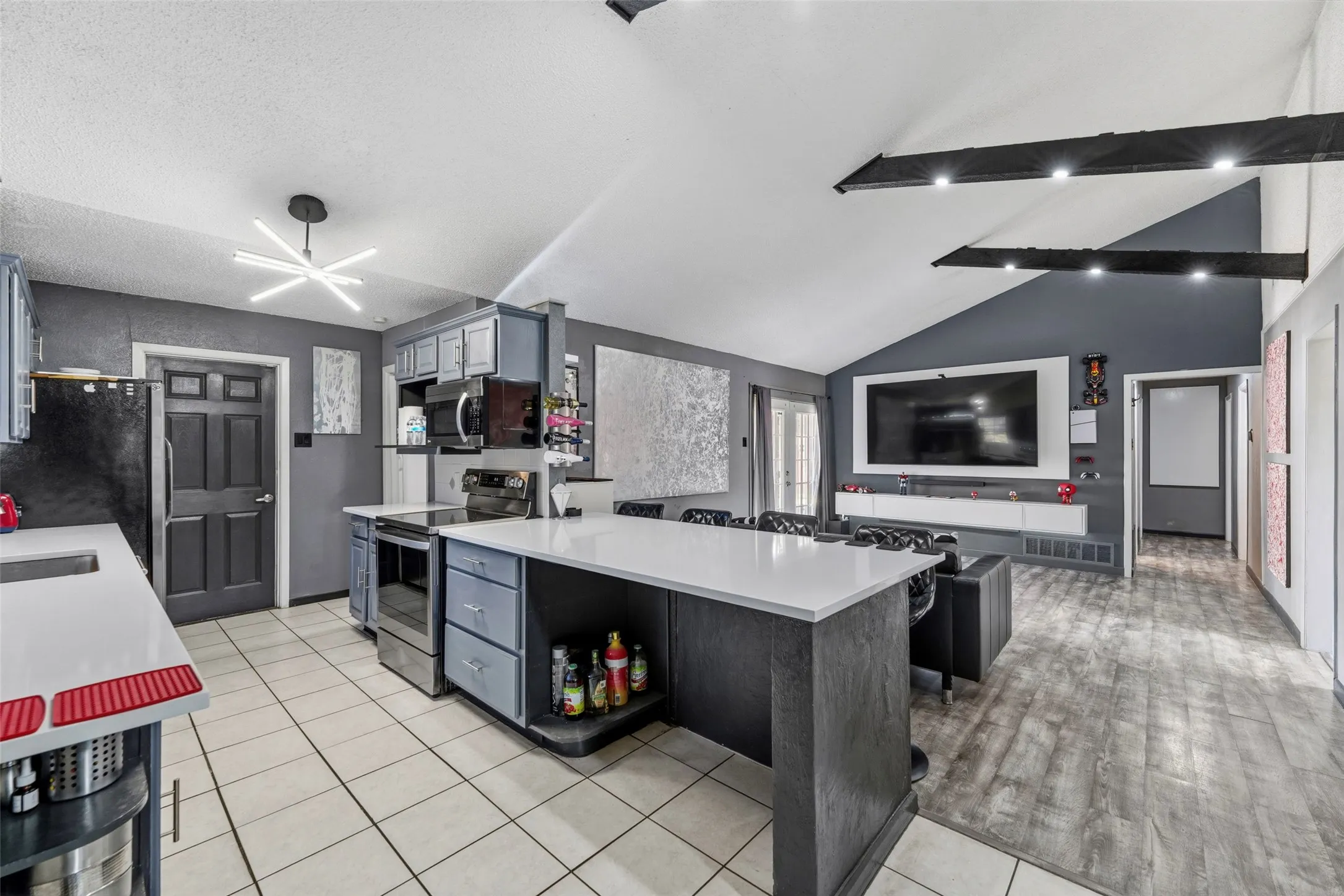 Vaulted ceiling with exposed beams, wood-finish flooring, white countertop island, stainless steel appliances, and ceiling-mounted light fixture