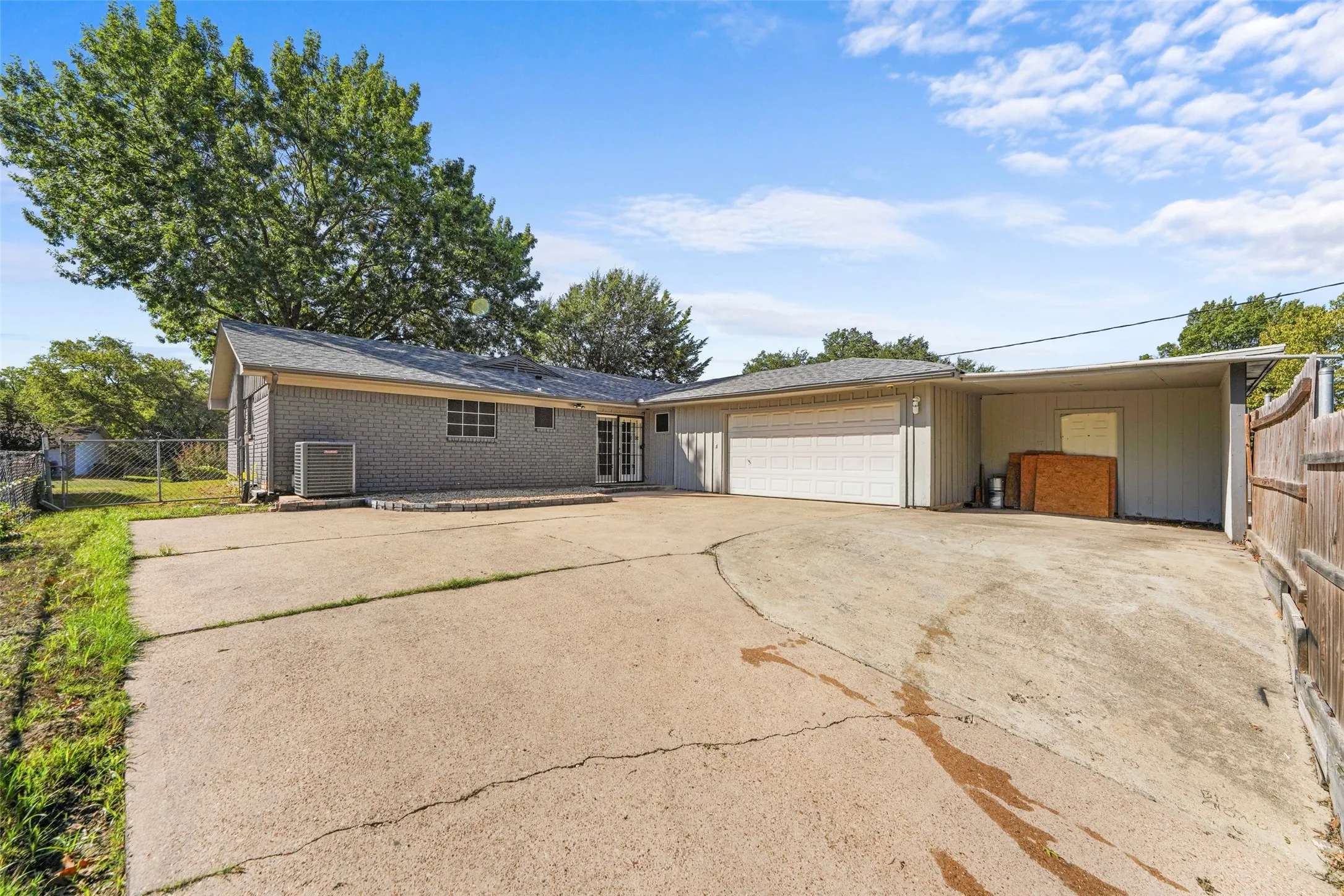 Gray brick exterior with a two-car garage, covered carport, and concrete drive