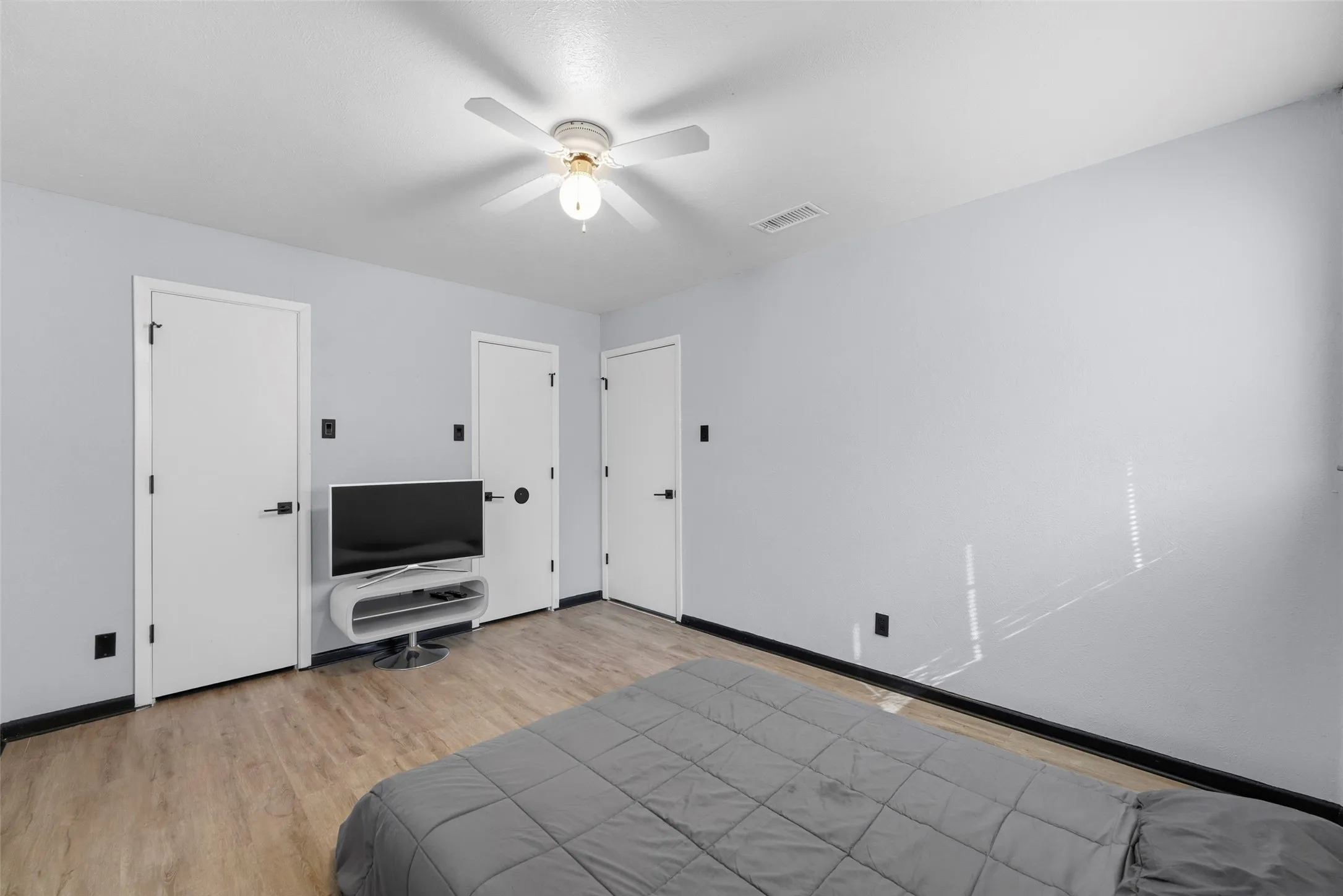 Wood-finish flooring, three white panel doors, and a ceiling fan with integrated lighting
