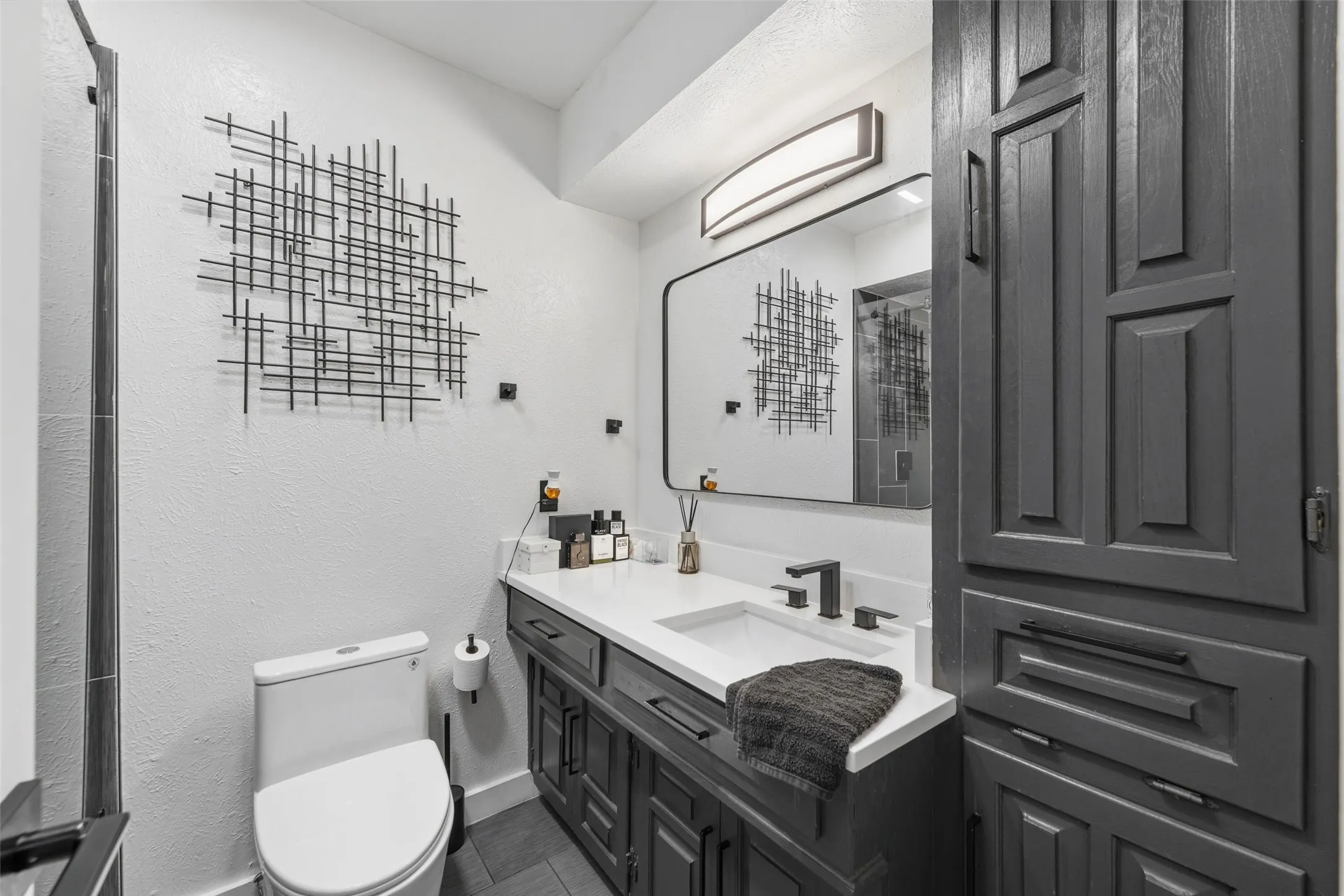 White vanity countertop with an integrated sink, dark wood-finish cabinetry, and matte black fixtures