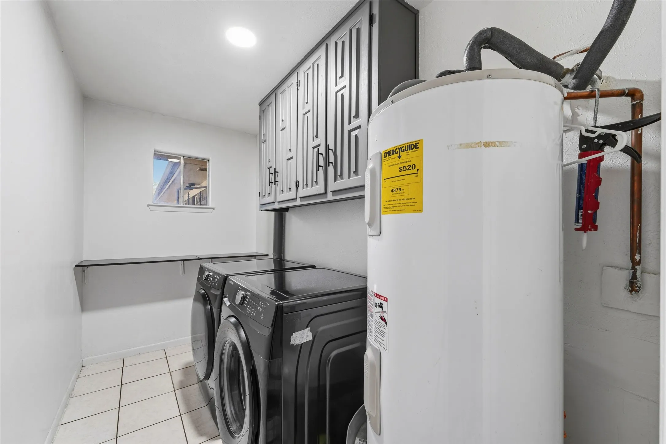 Laundry area featuring white walls, tile flooring, built-in upper cabinetry, and a floating wall shelf