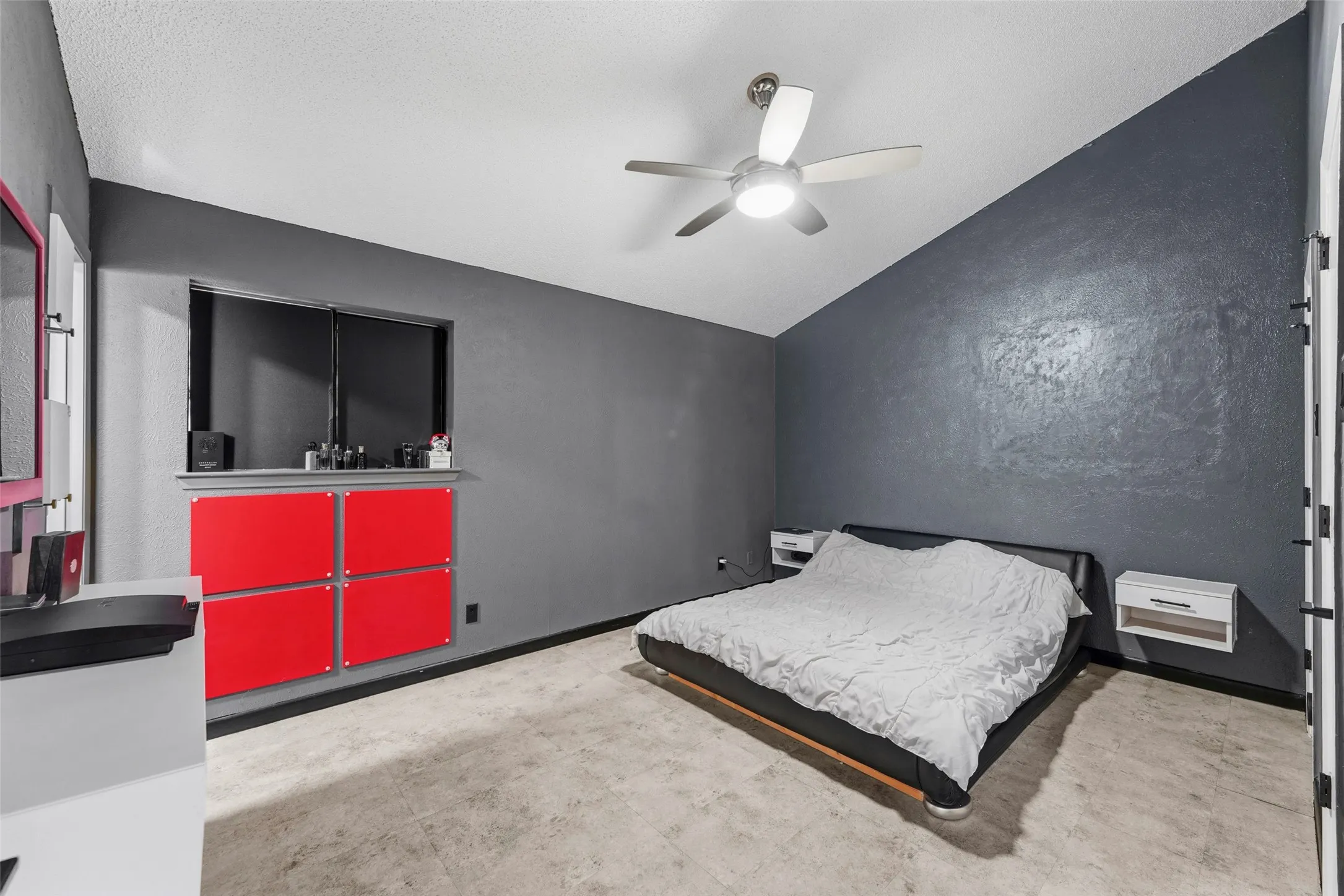 Sloped ceiling, ceiling fan with integrated lighting, window with built-in storage below, red wall-mounted cabinetry, and wood-finish flooring