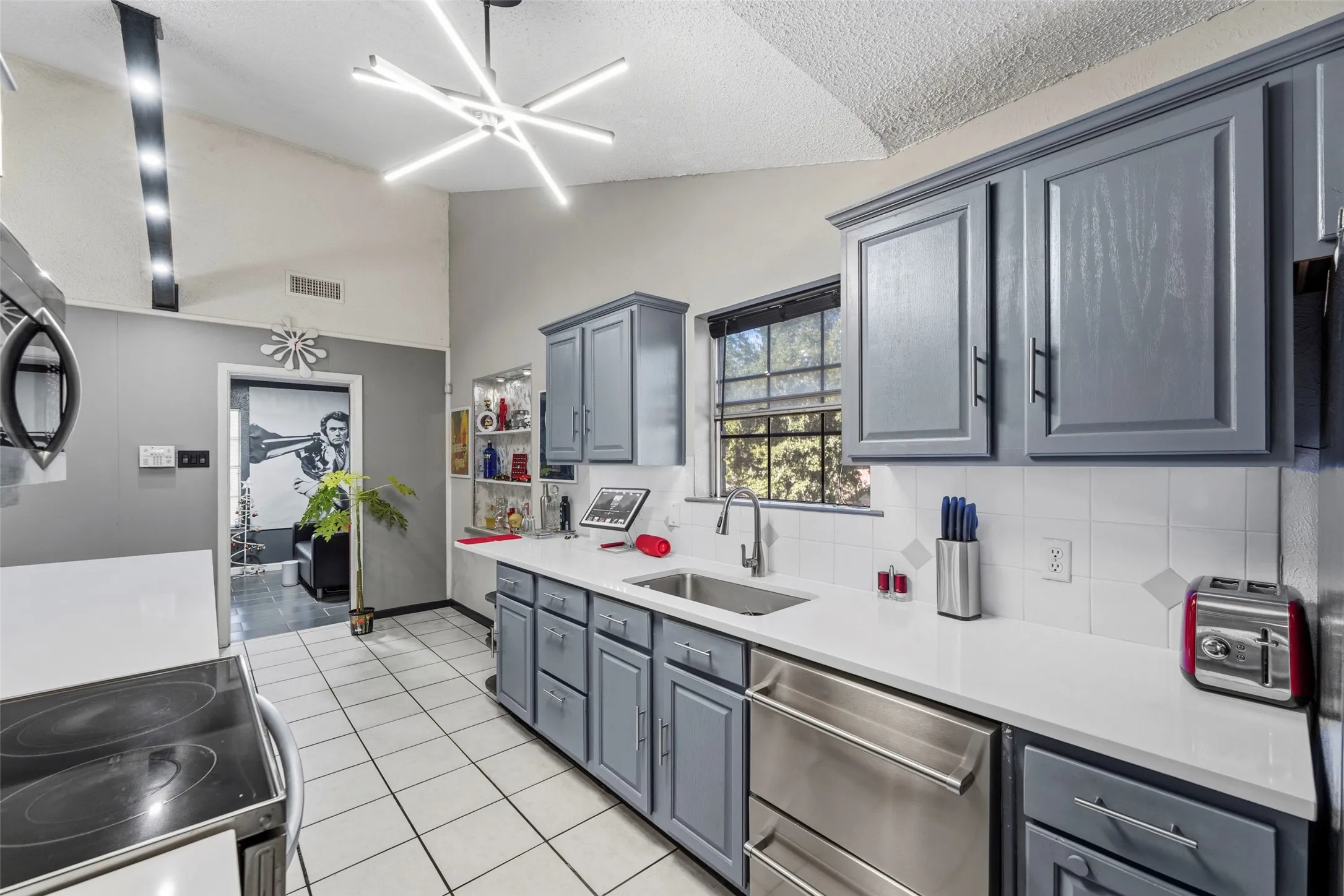 Vaulted ceiling, contemporary linear chandelier, shaker-style cabinetry, white countertops, and stainless steel appliances