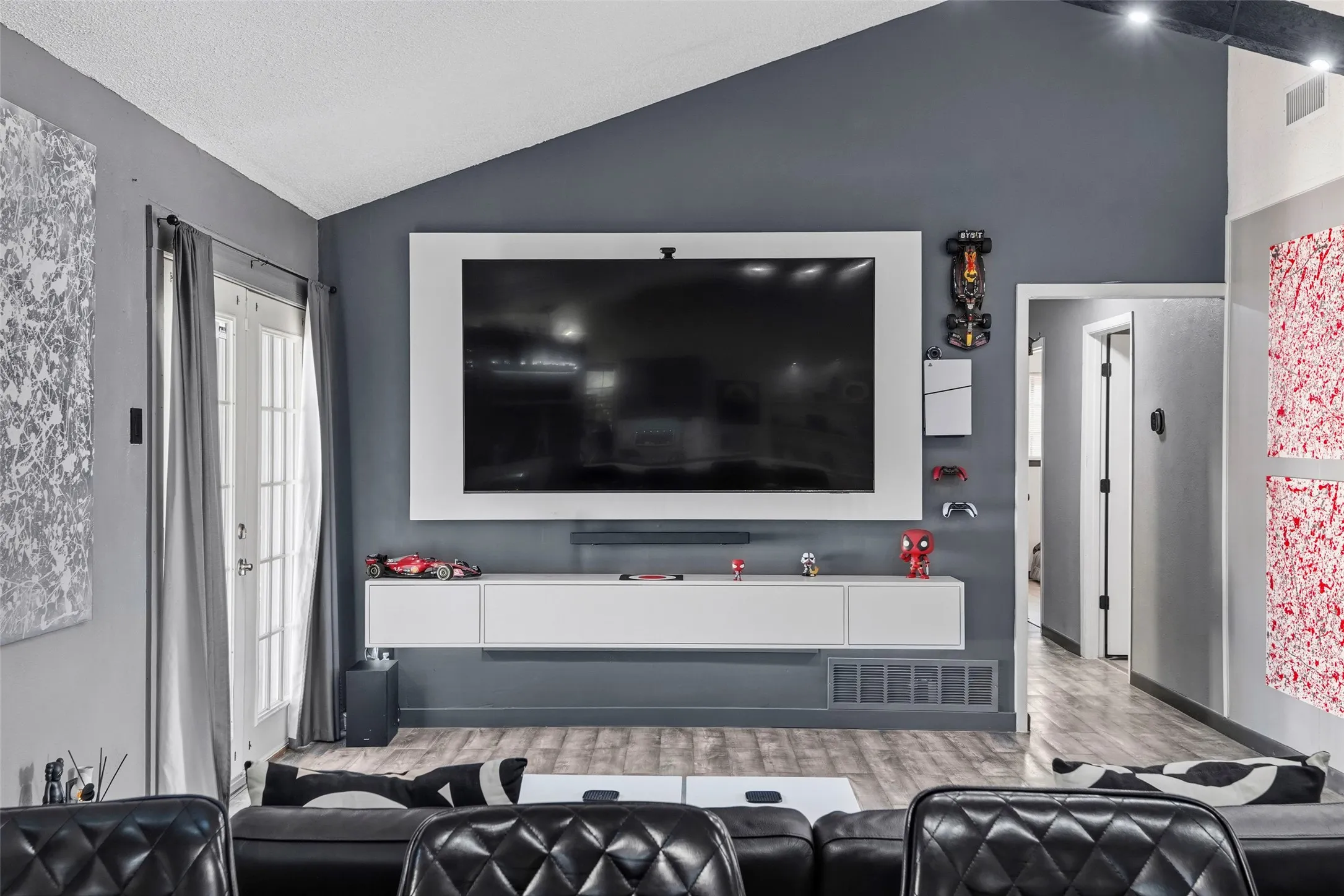 Vaulted ceiling, wood-finish flooring, white double French doors, white framed media wall, and a floating entertainment console
