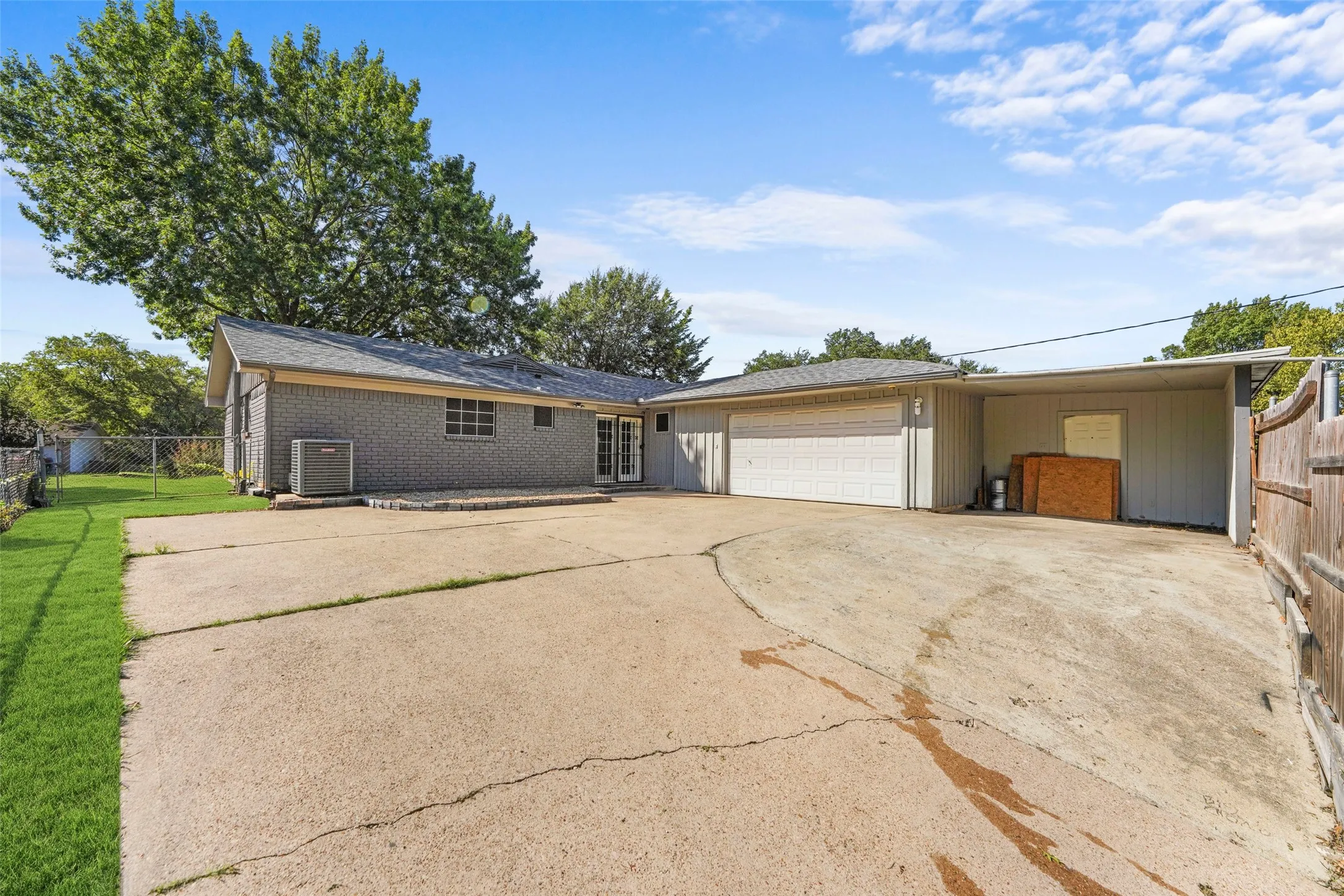 Brick exterior with a gabled roofline, attached garage, covered carport, and concrete driveway
