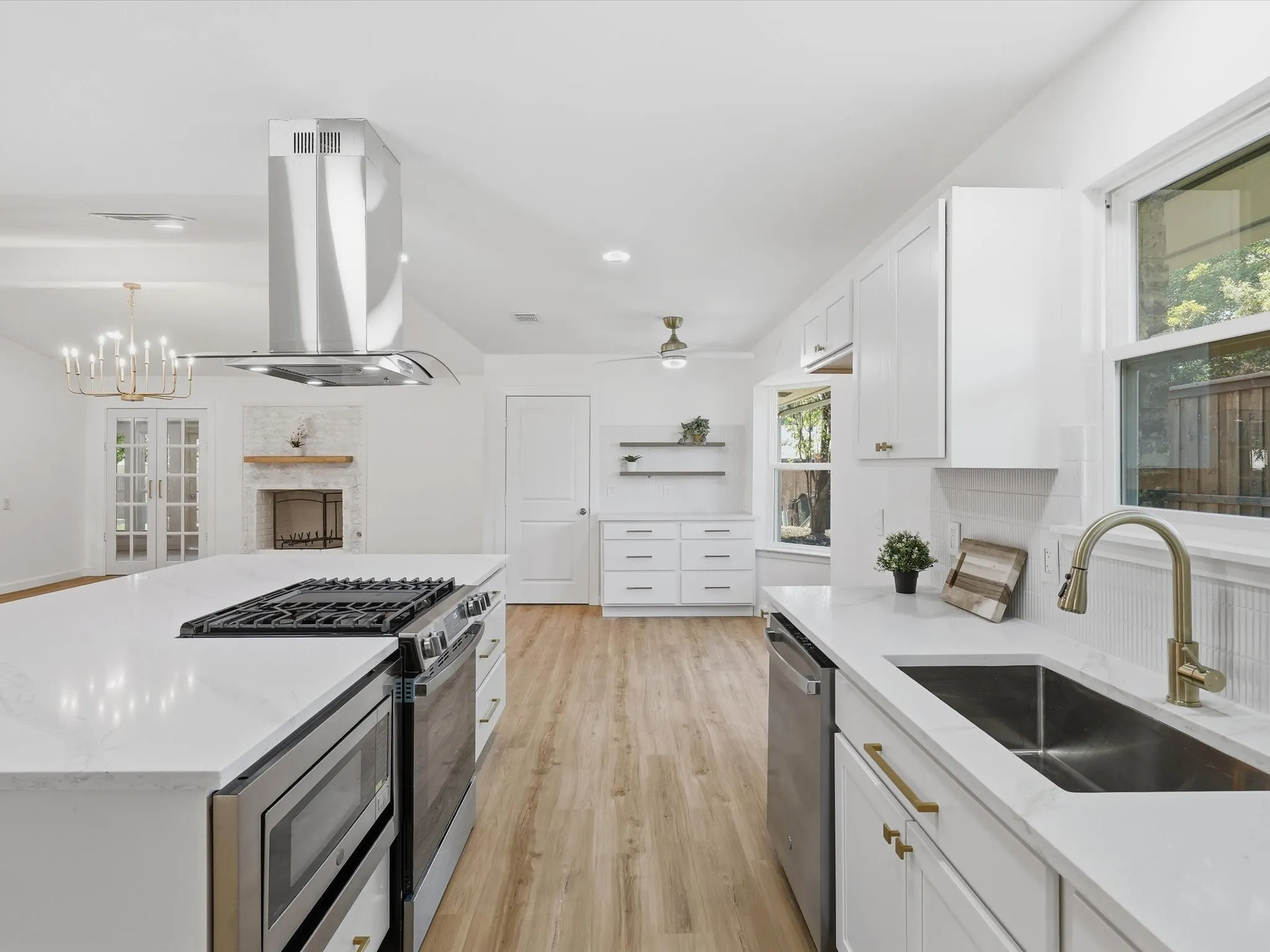 Spacious kitchen featuring an island with built-in range, stainless steel appliances, white cabinetry, and wood-finish flooring