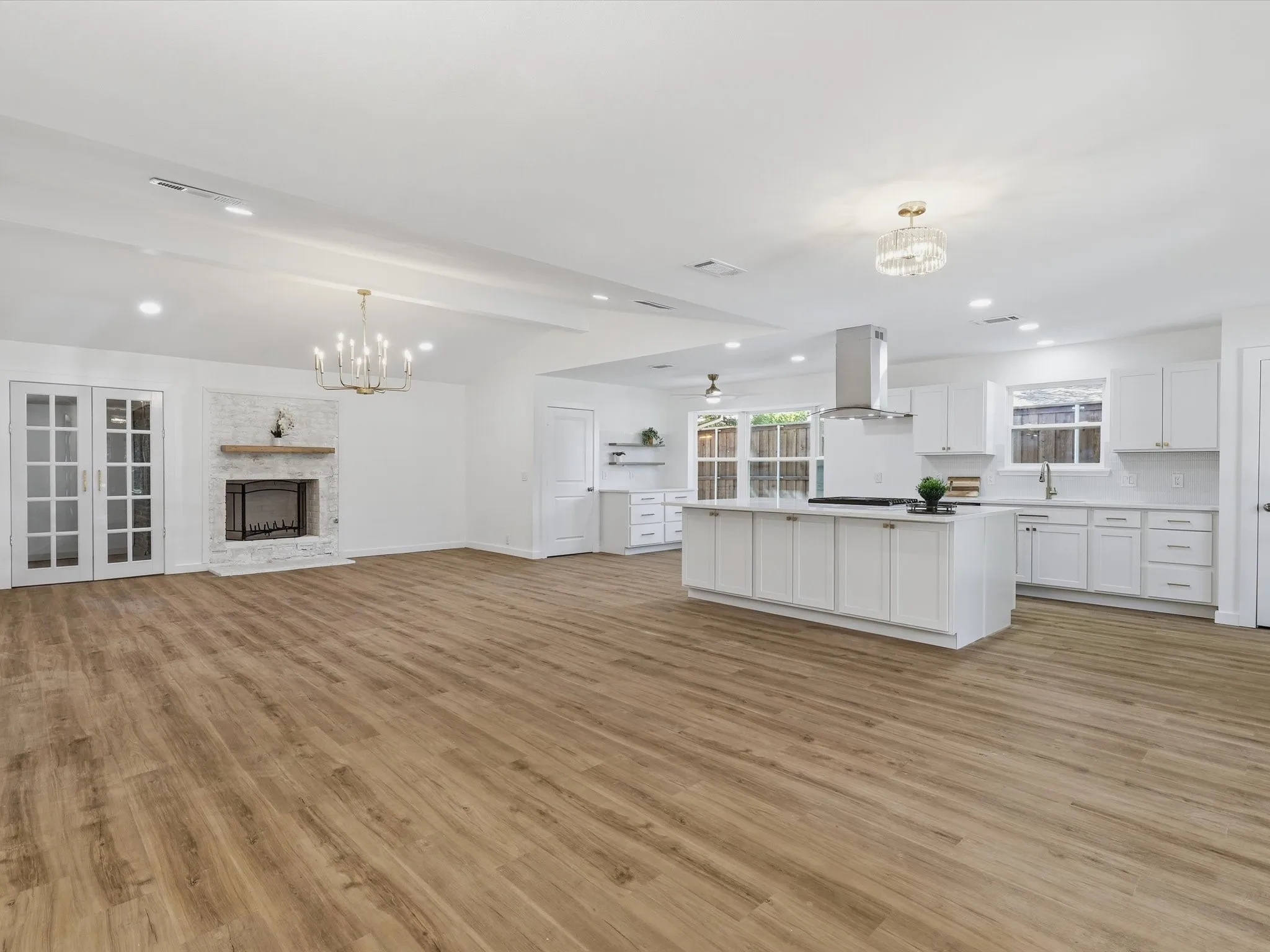 Expansive open-concept space featuring wood-finish flooring, a white brick fireplace with a wood mantel, and double French doors