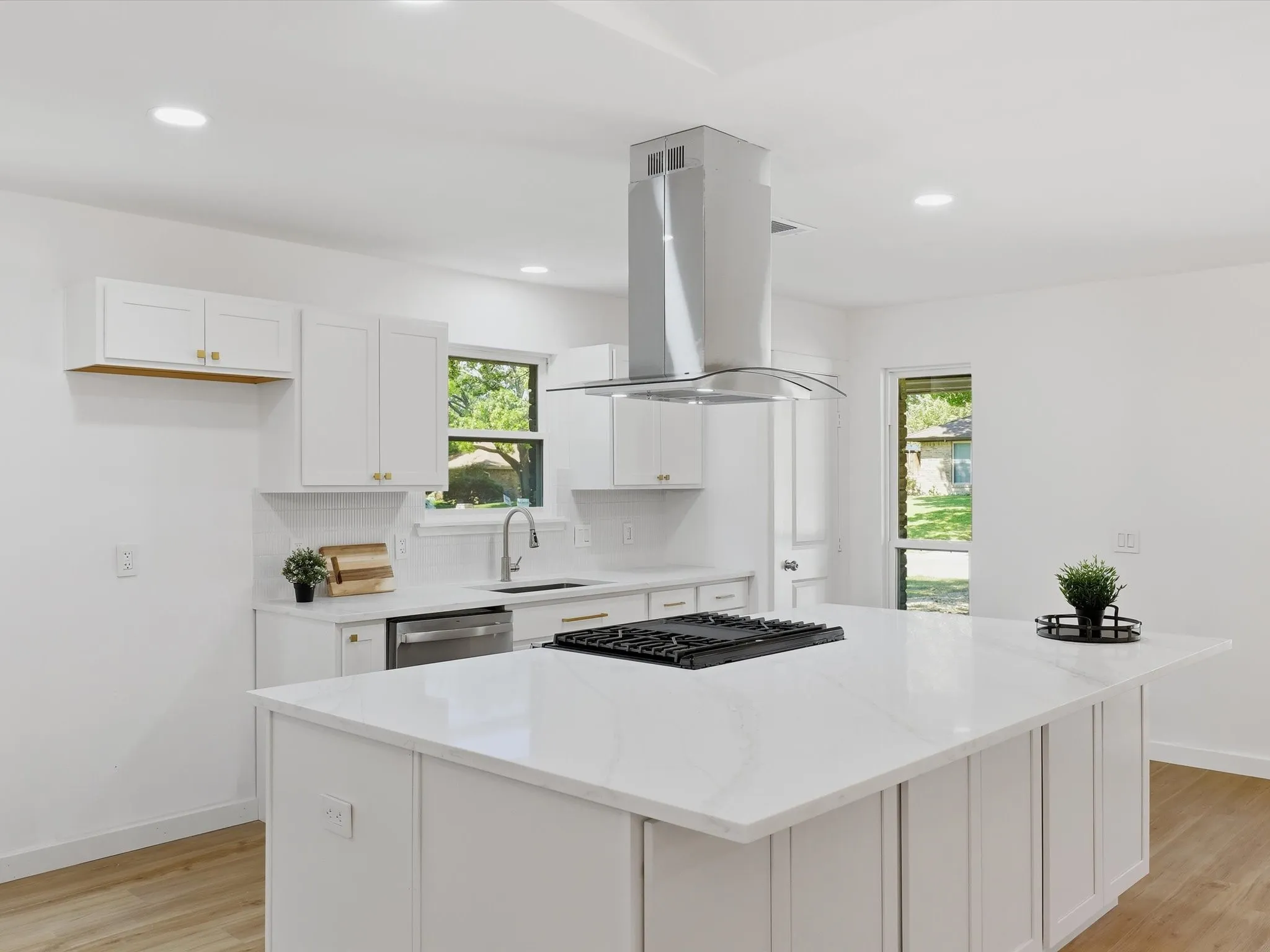 White shaker cabinetry with gold-finish hardware, stainless steel appliances, white subway tile backsplash, white countertop island with integrated cooktop, and wood-finish flooring