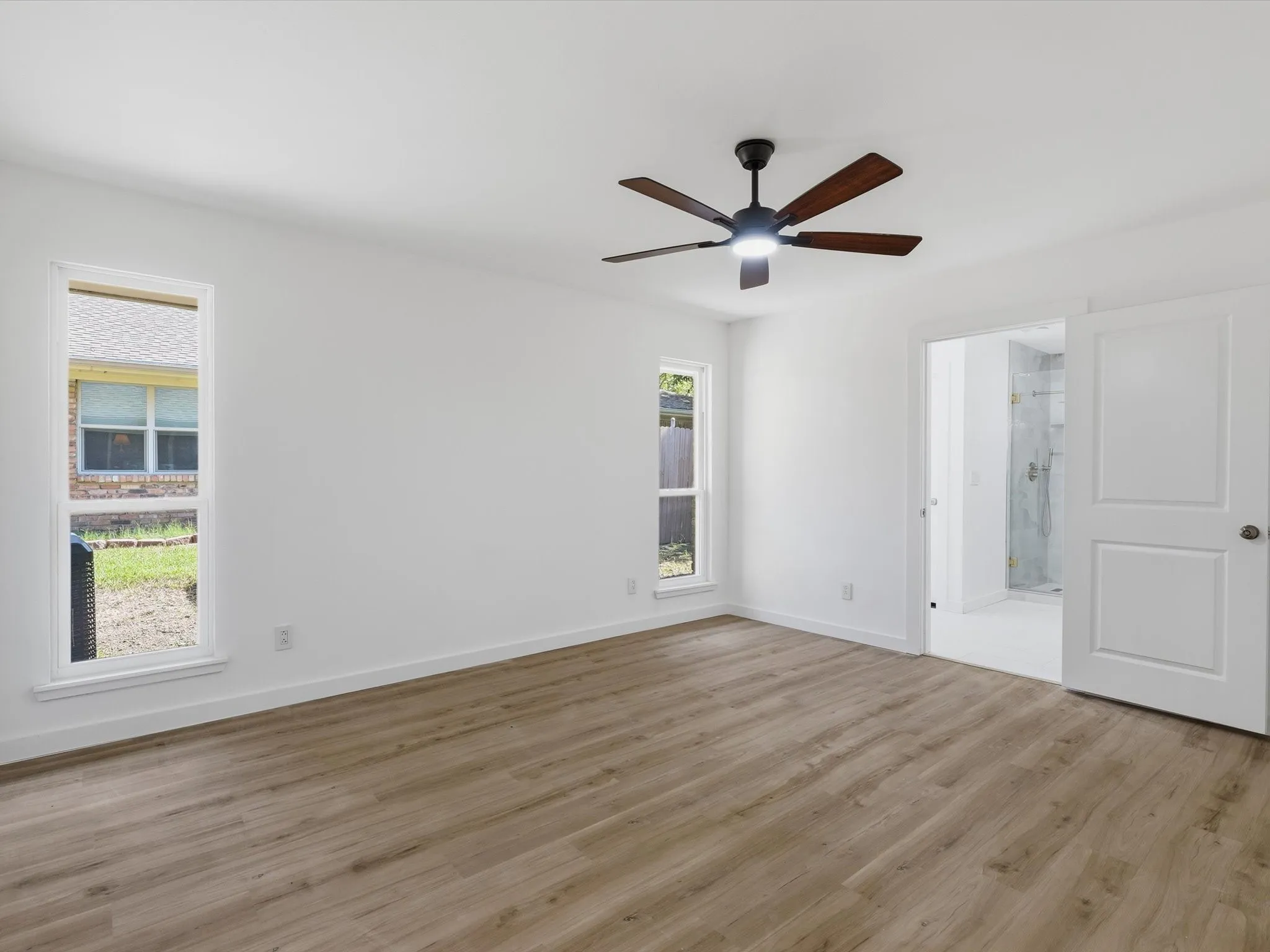 Spacious room featuring wood-finish flooring, white walls, and a ceiling fan with integrated lighting