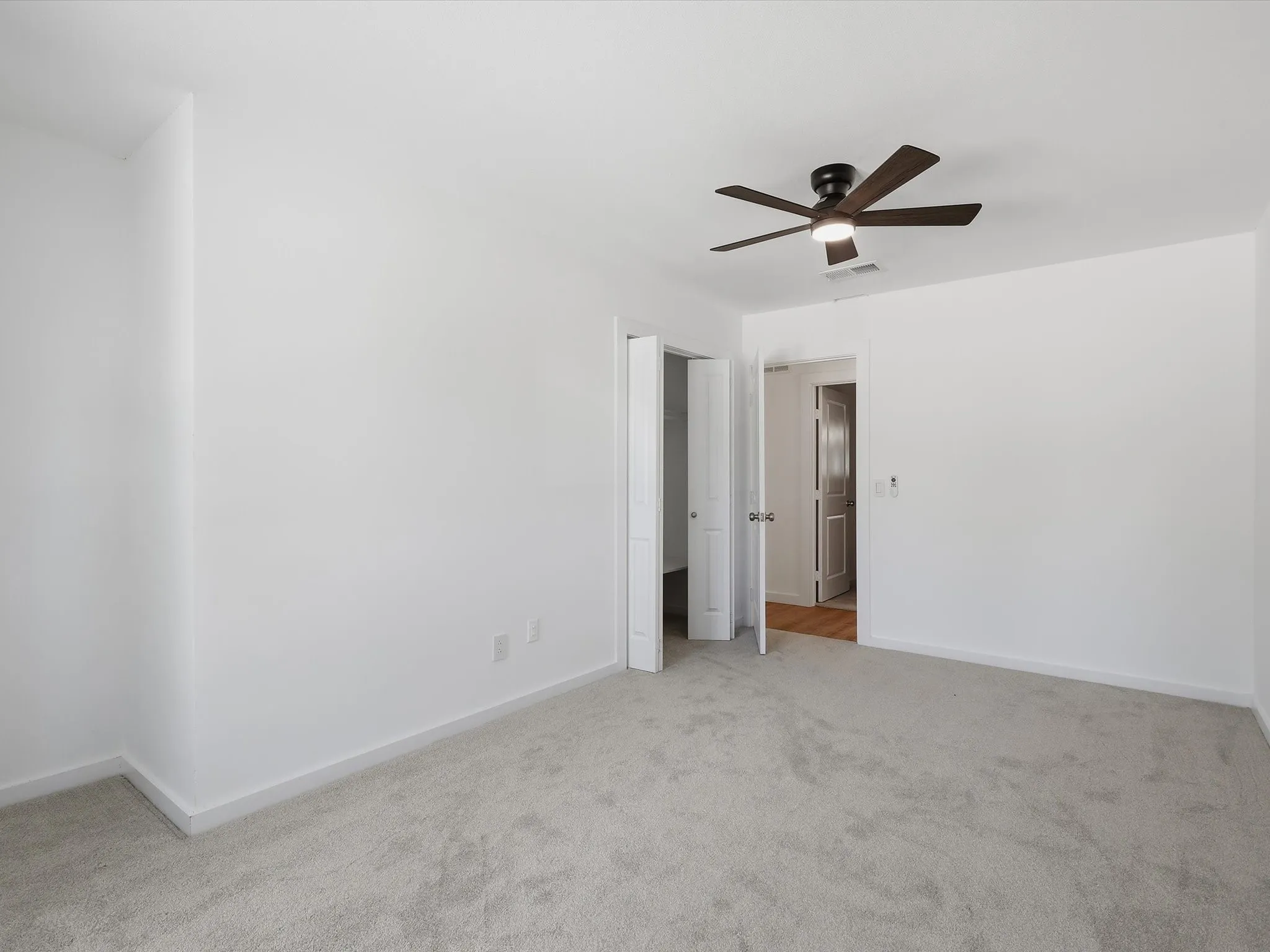 Plush carpet flooring, a ceiling fan with integrated lighting, and white walls