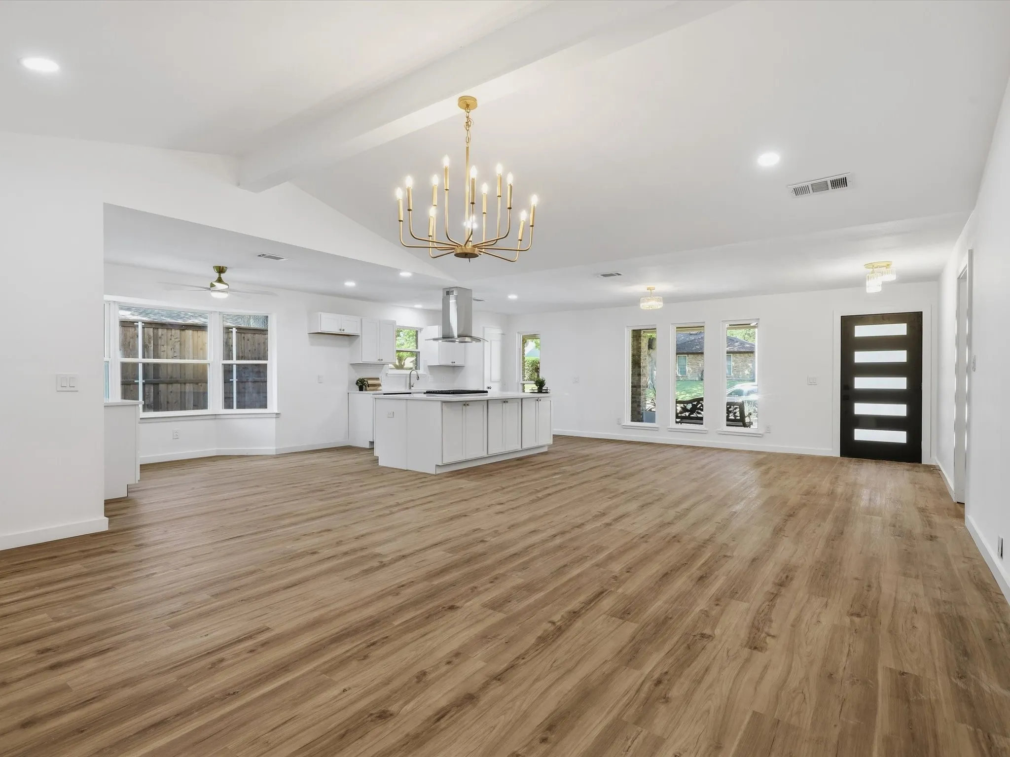 Vaulted ceilings, wood-finish flooring, central island kitchen, modern black entry door, and multiple windows