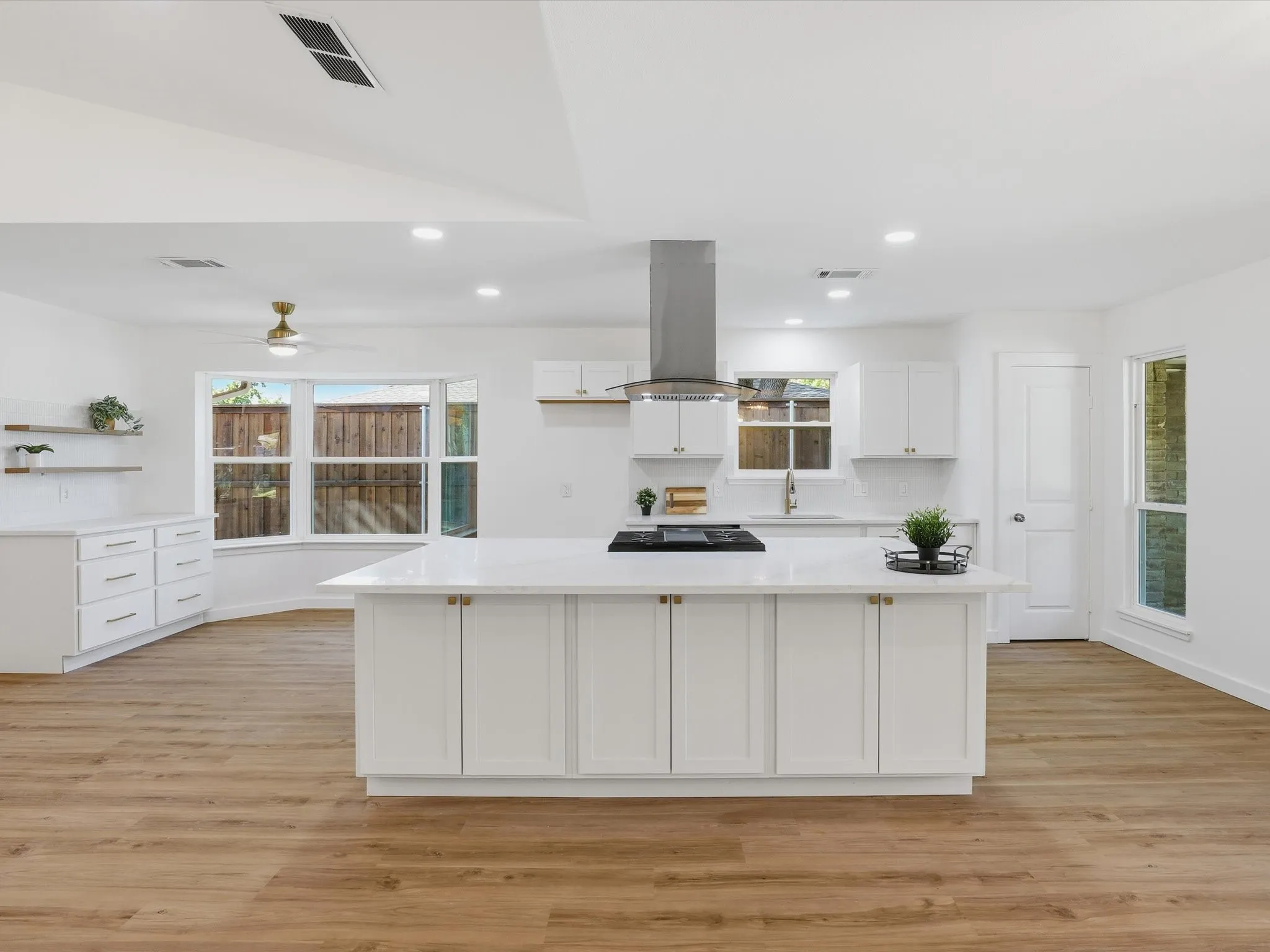 Open-concept kitchen featuring an island with a cooktop, wood-finish flooring, white cabinetry, and recessed lighting