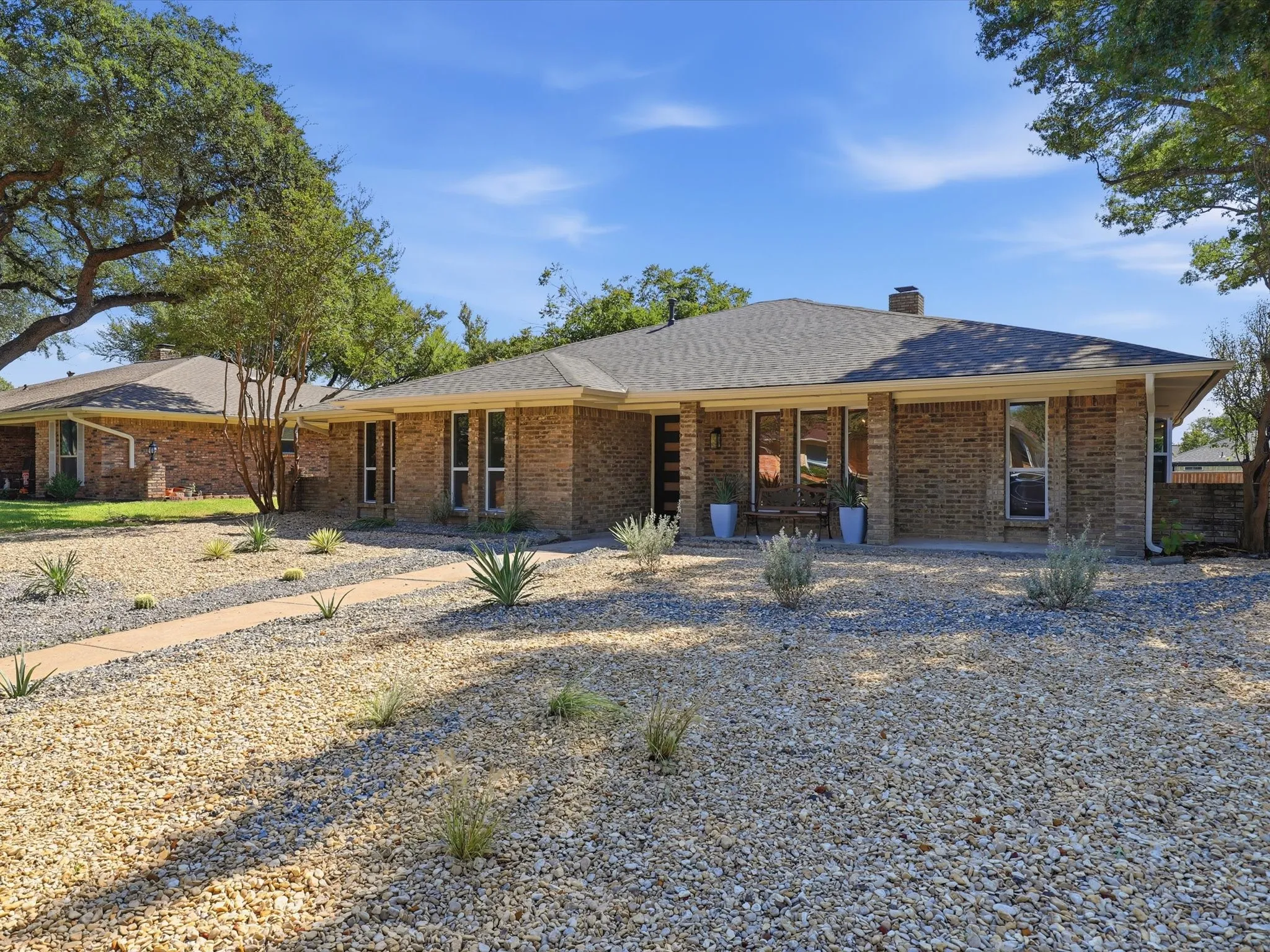 Brick exterior with a gray shingle roof, complemented by a gravel and xeriscape front yard featuring a paved walkway