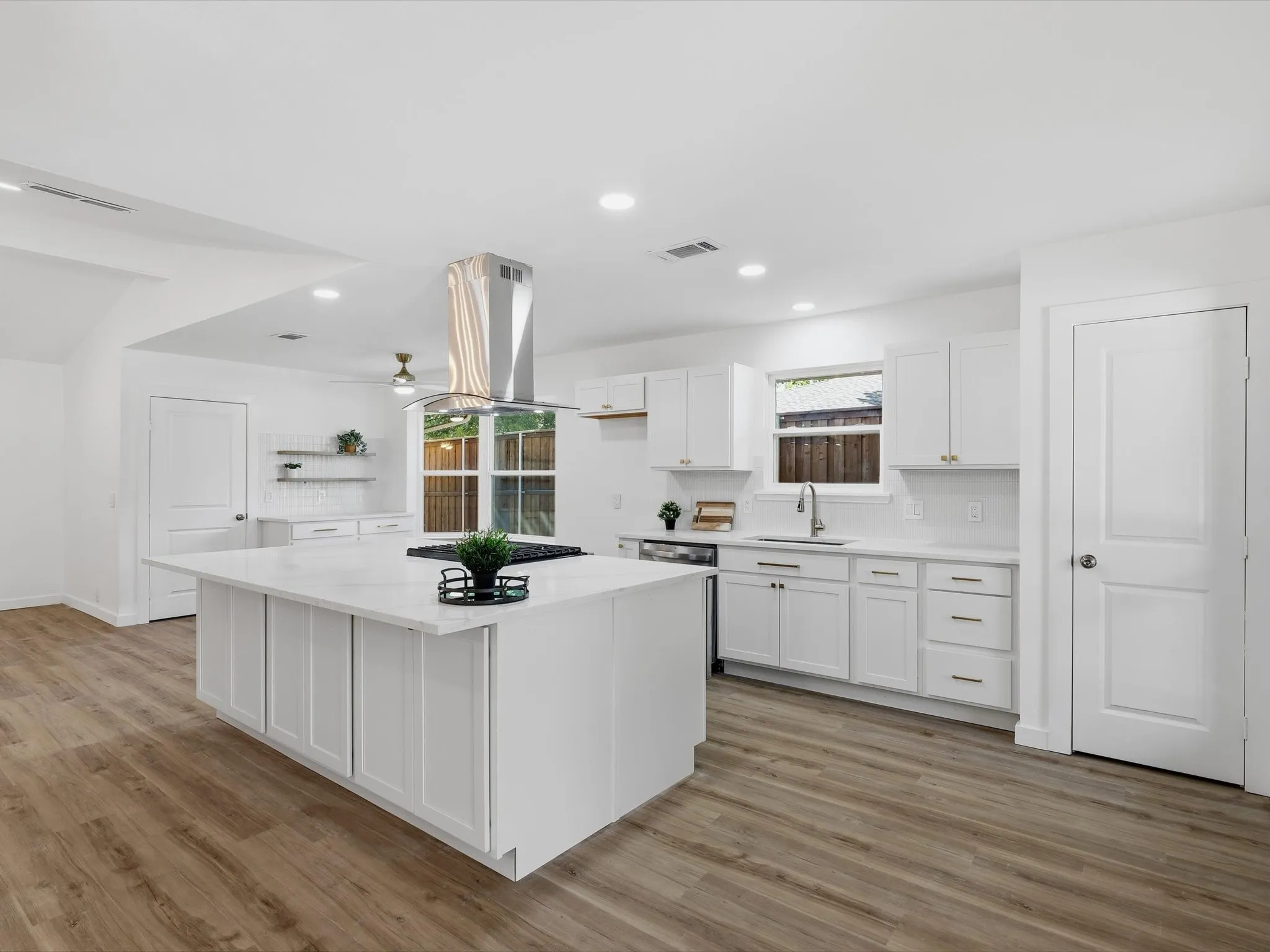 White kitchen featuring a large island with a cooktop, stone countertops, white shaker-style cabinetry, and wood-finish flooring