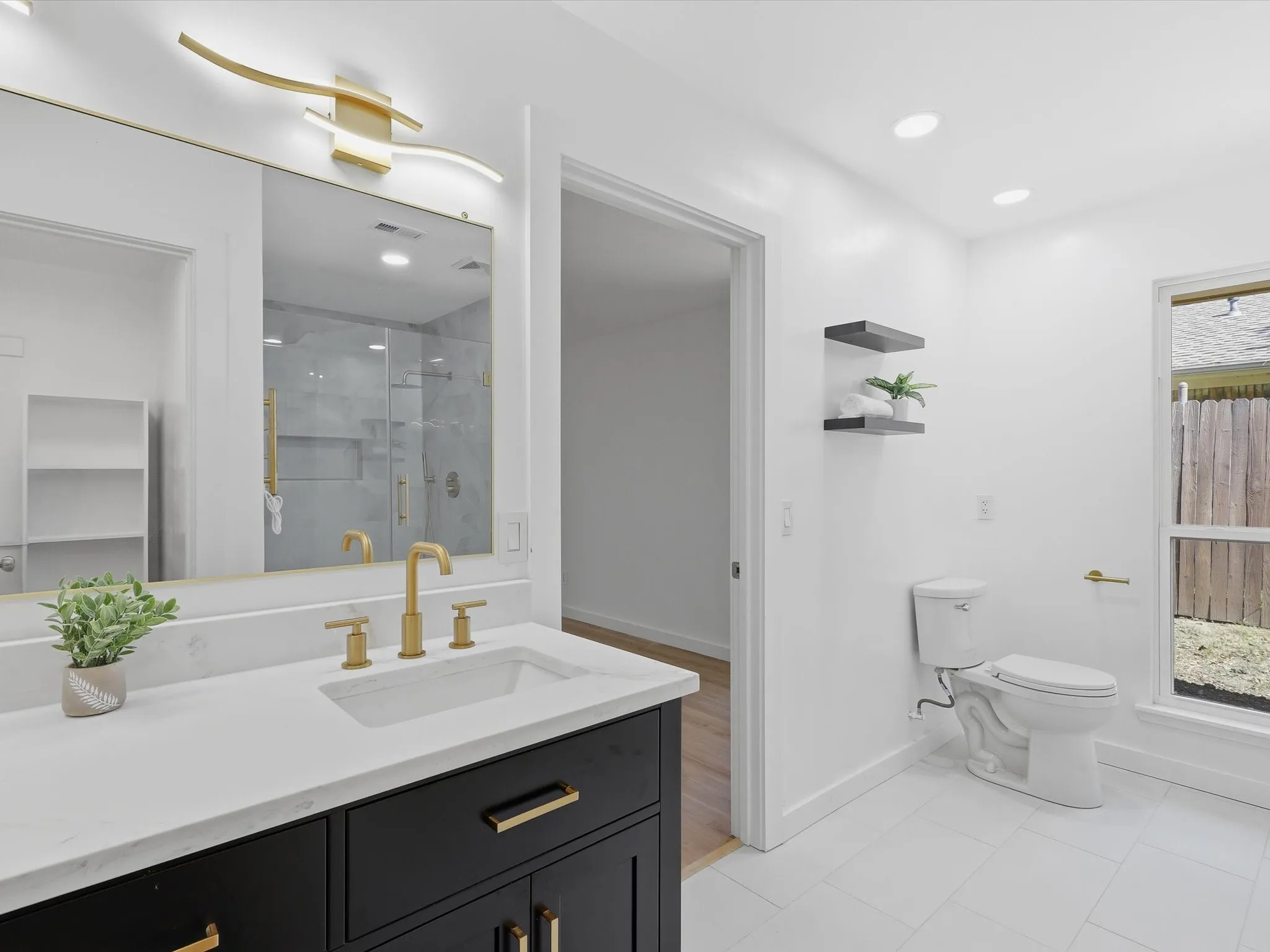 Modern bathroom featuring a black vanity with a white countertop, gold-finish fixtures, and white tile flooring