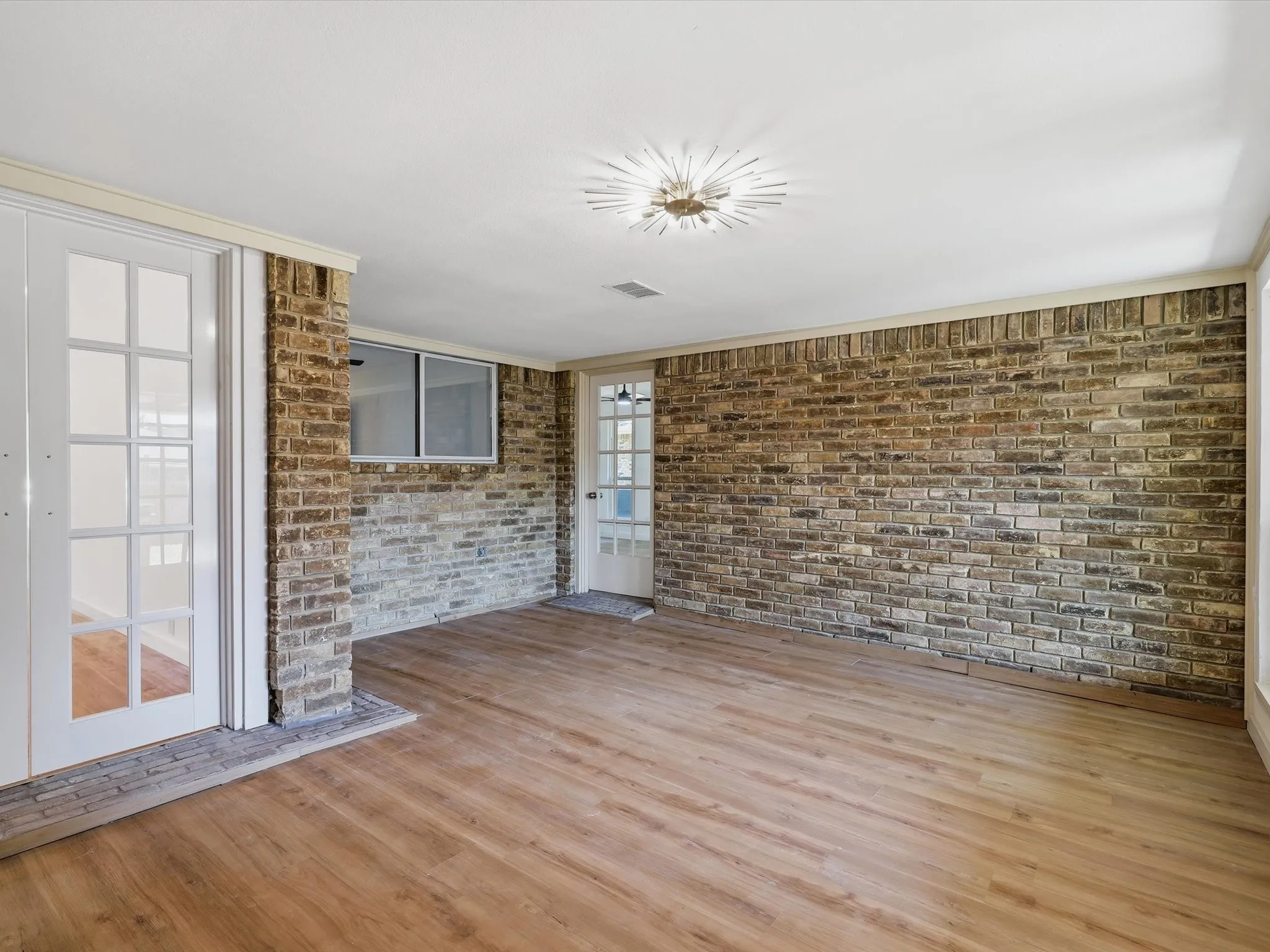 Wood-finish flooring, exposed brick wall, white French doors, and recessed lighting