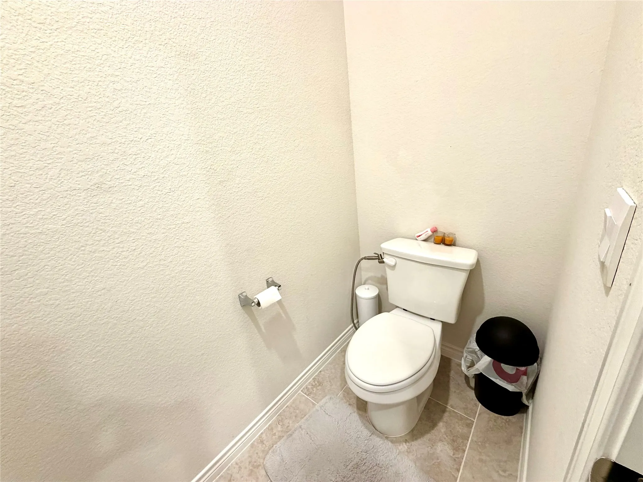 White commode with a bidet attachment, light-toned textured walls, and tiled flooring